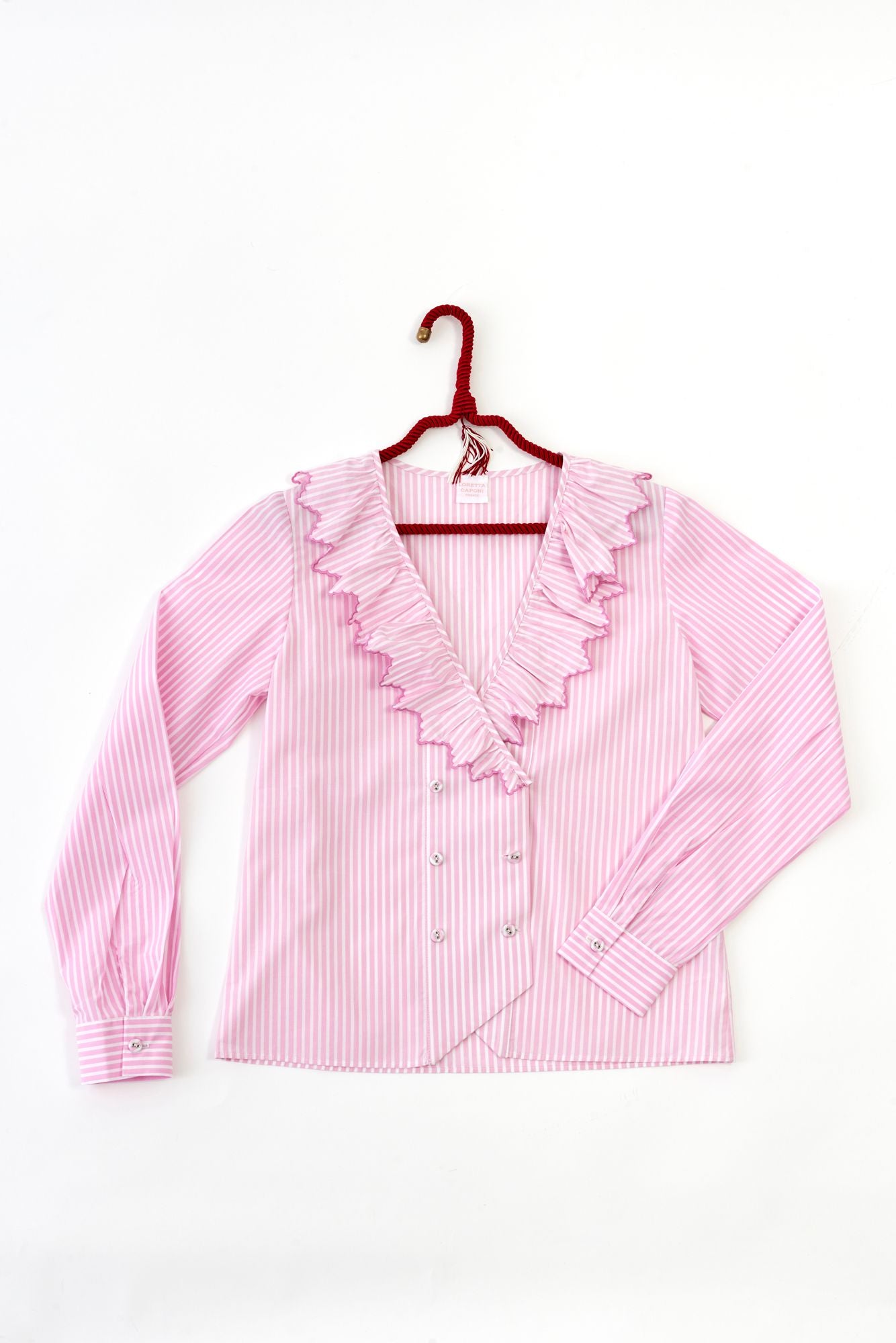 Pink striped blouse with ruffled details on a hanger against a white background