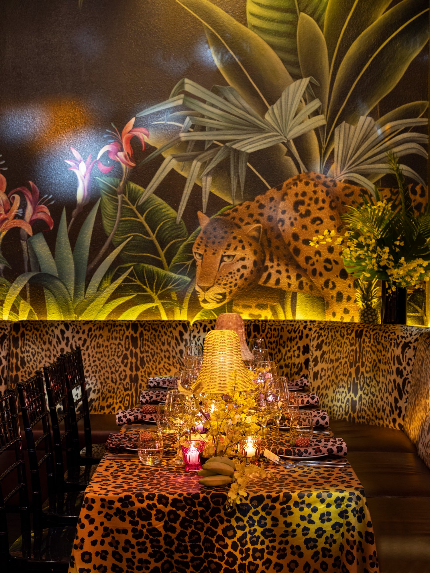 Elegant table setting against tropical backdrop with cheetah print tablecloths, woven lamp shades, and low lighting for a private party.