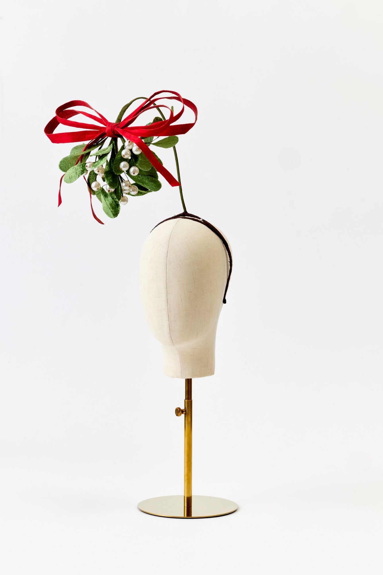 Mannequin head with a red bow and mistletoe headband on a white background