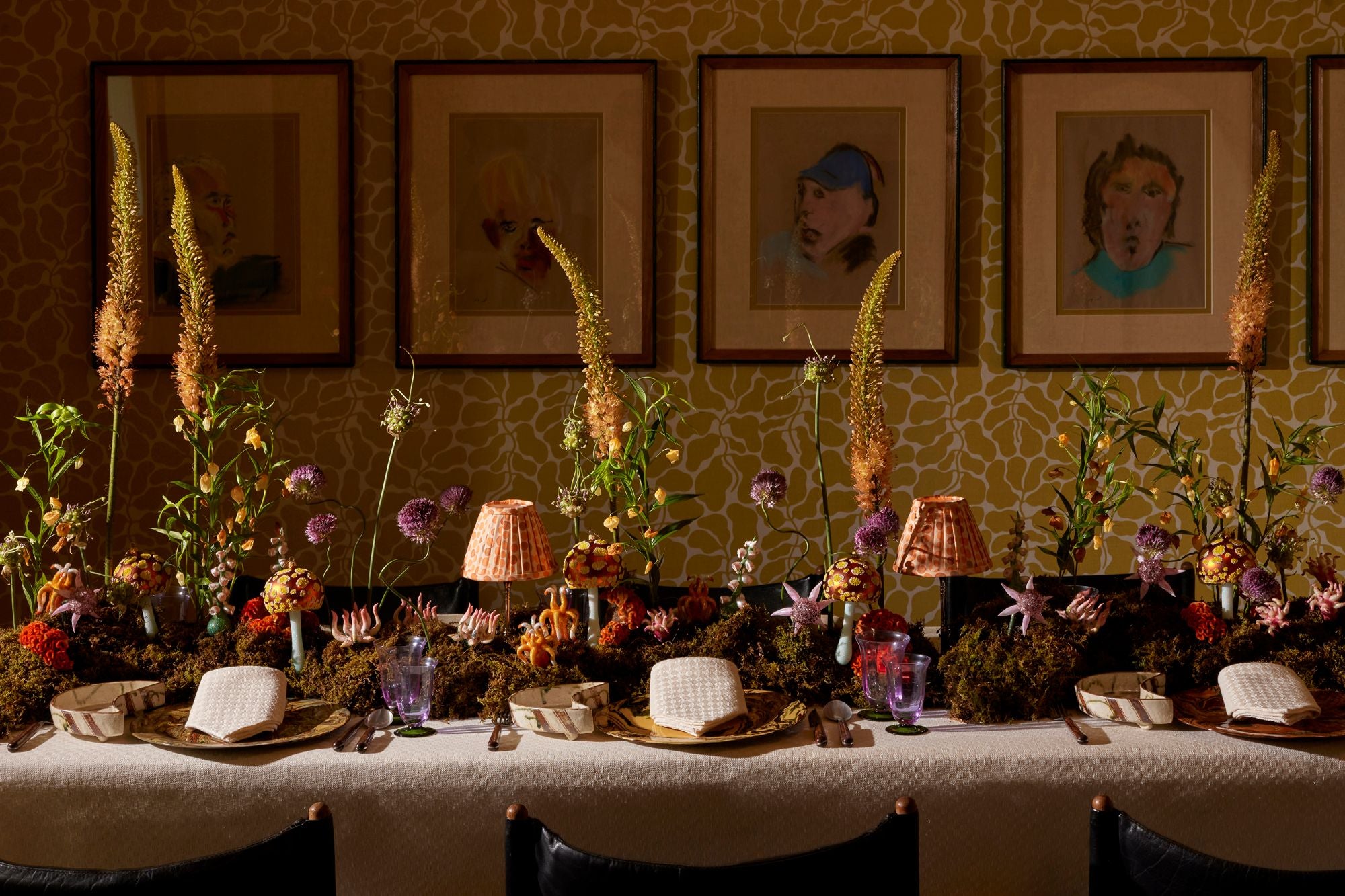 Decorative table setting with flowers, candles, and framed pictures on a patterned wall.