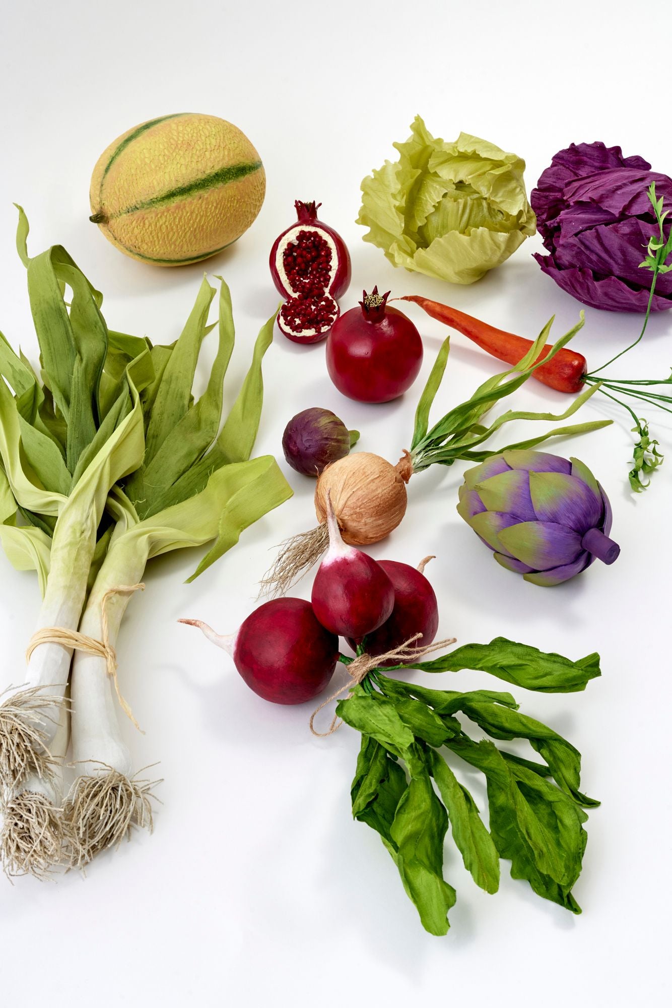 Assorted silk vegetables including radishes, artichokes, and a cantaloupe on a white background