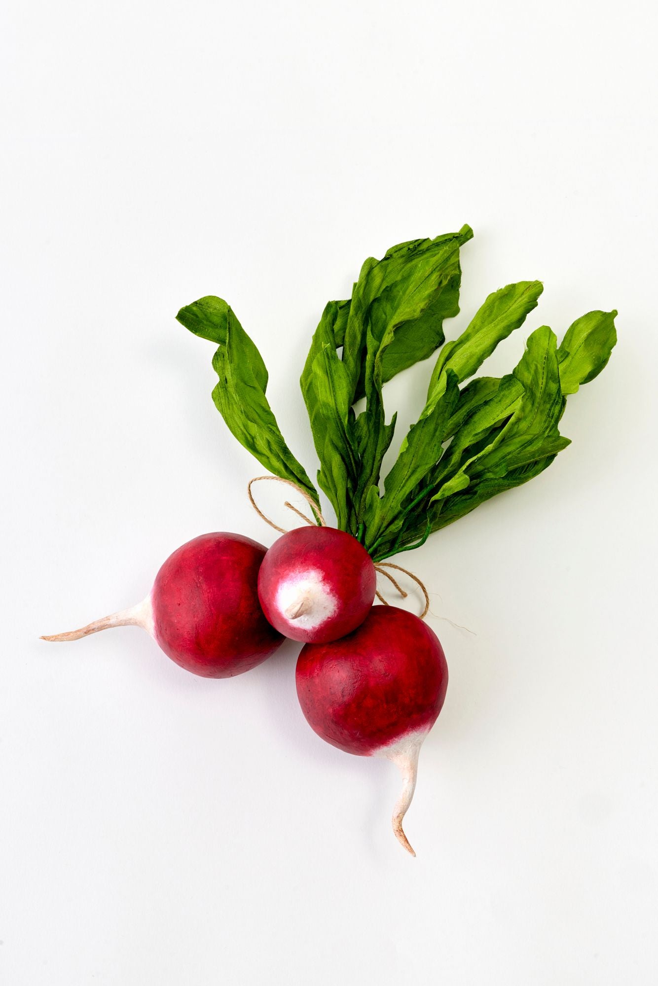 Three red silk radishes with green leaves on a white background