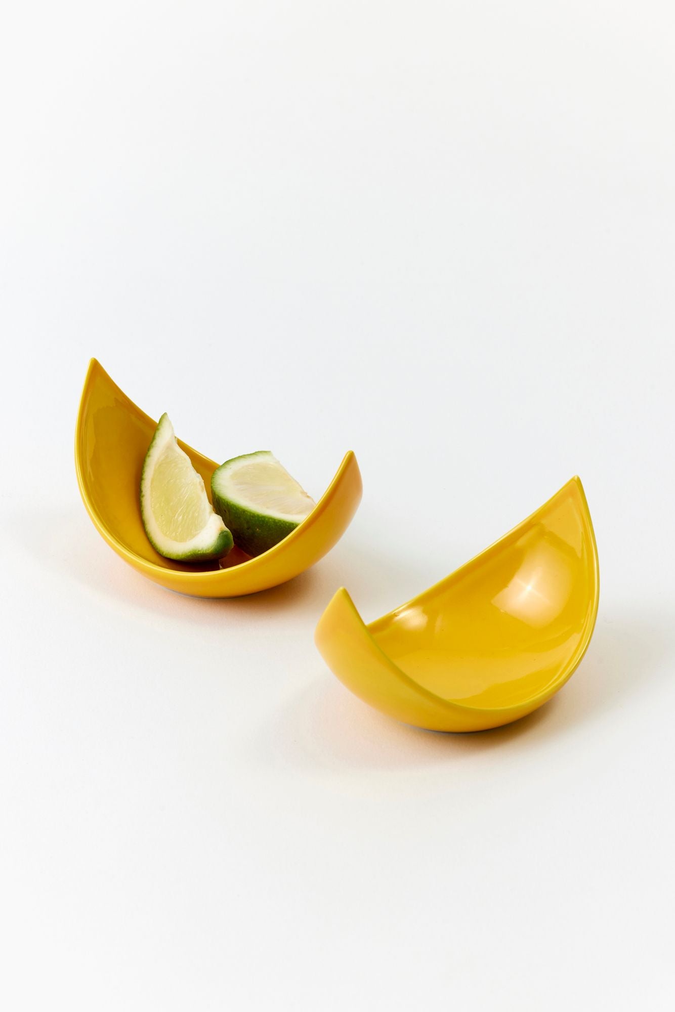 Yellow ceramic wedge bowl with sliced limes on a white background