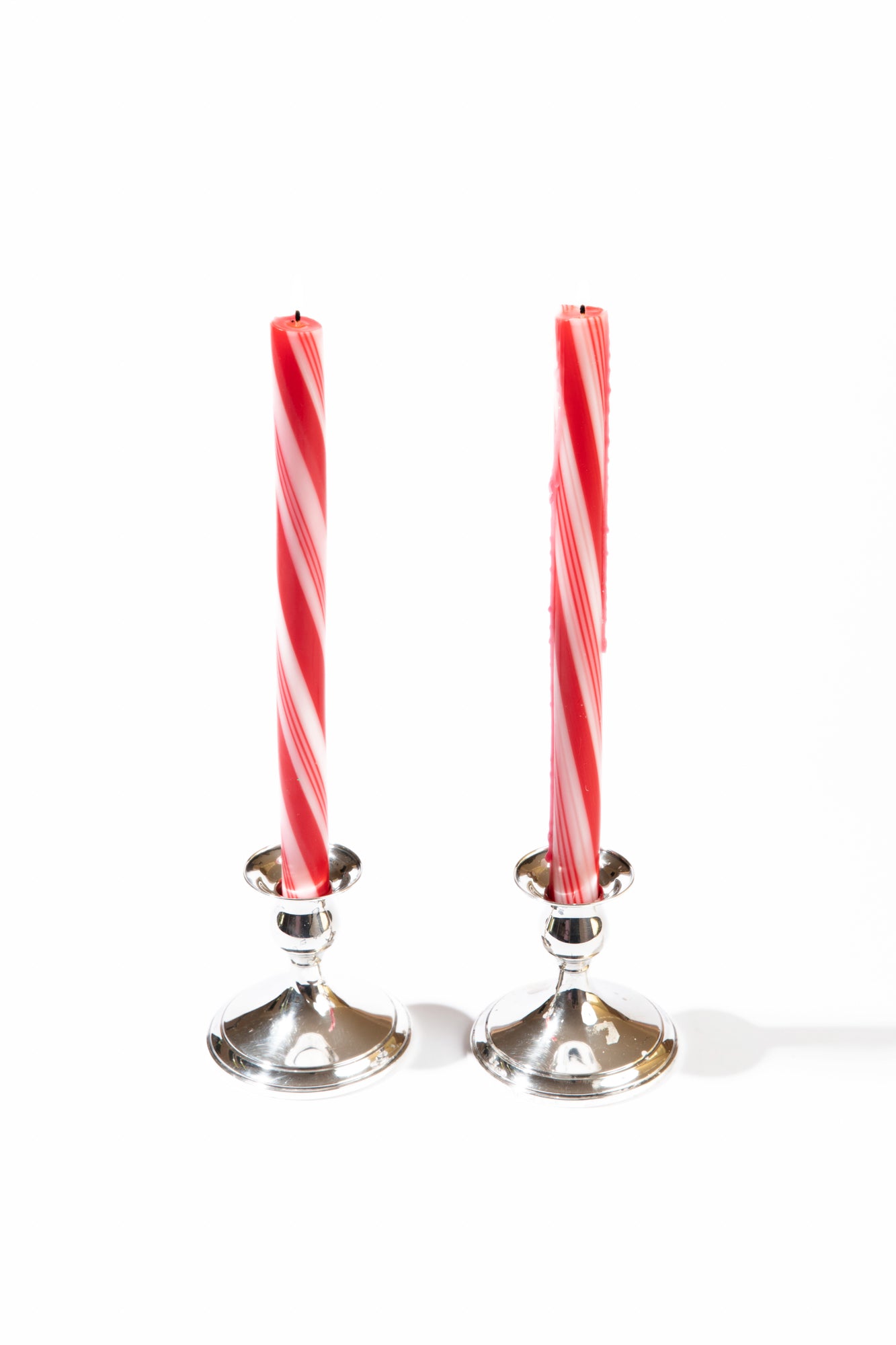 Photograph of two 12 inch taper candles with a red and white peppermint twist design, each placed in silver candlestick holders.