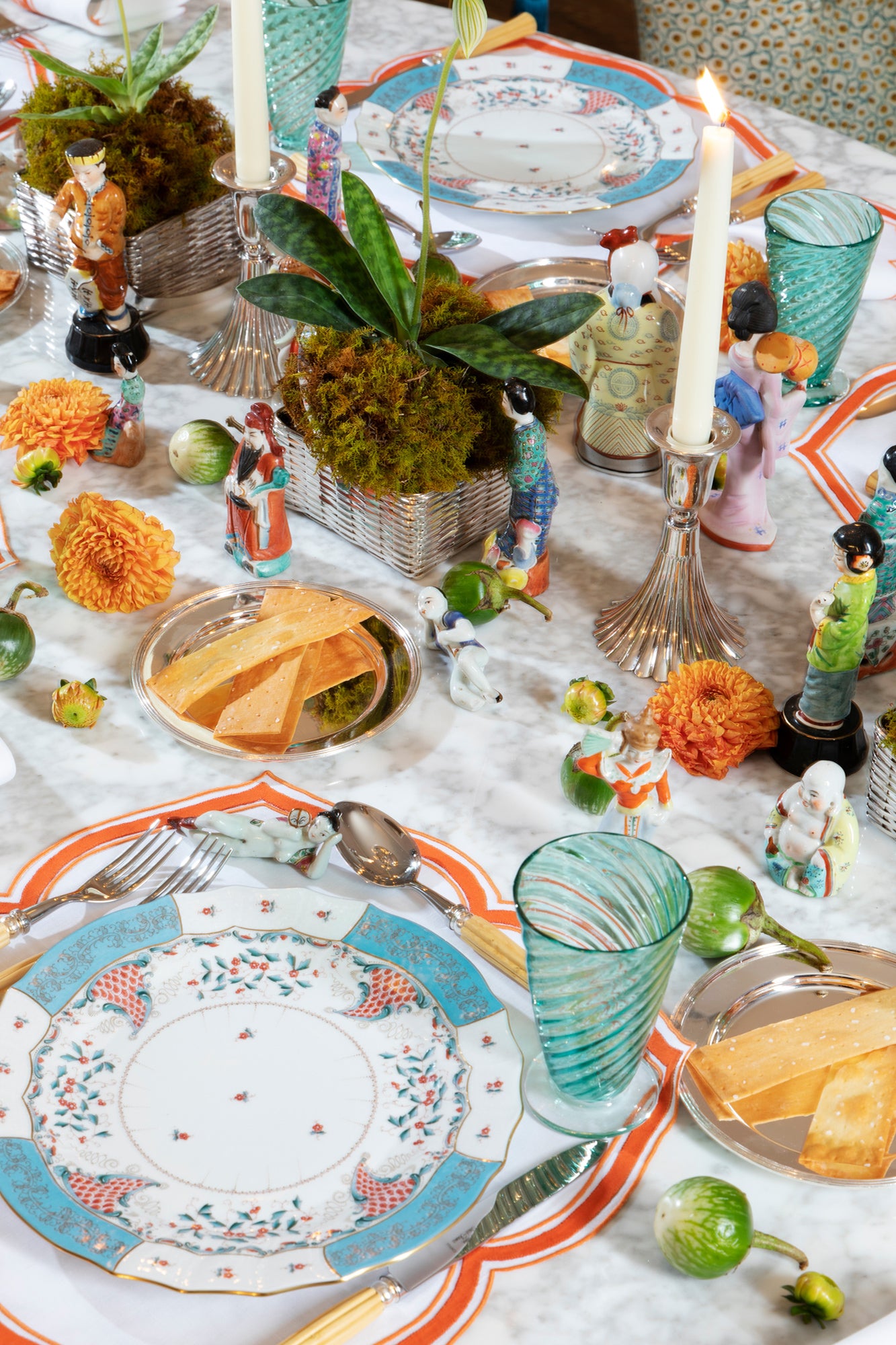 Close up photograph of table setting featuring Herend Cornucopia dinner plates, hand blown glass twist goblets, silver bread plates, porcelain figurines, ivory taper candles, and fresh flowers.