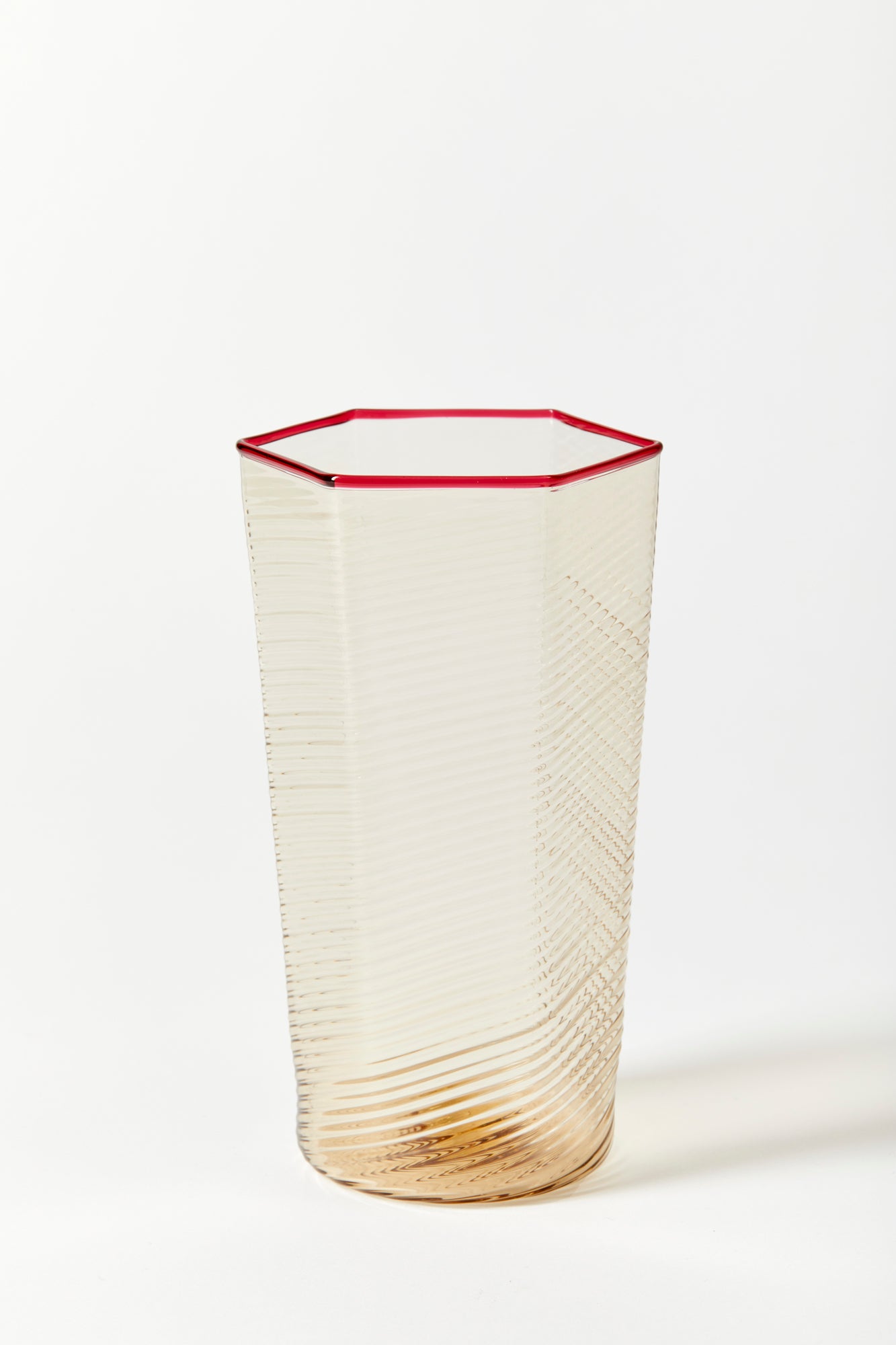 Fine and delicately striated hexagonal glass for everyday use. Handblown and molded by artisans in Murano. The neutral warm smoke color complements the thin red rim.