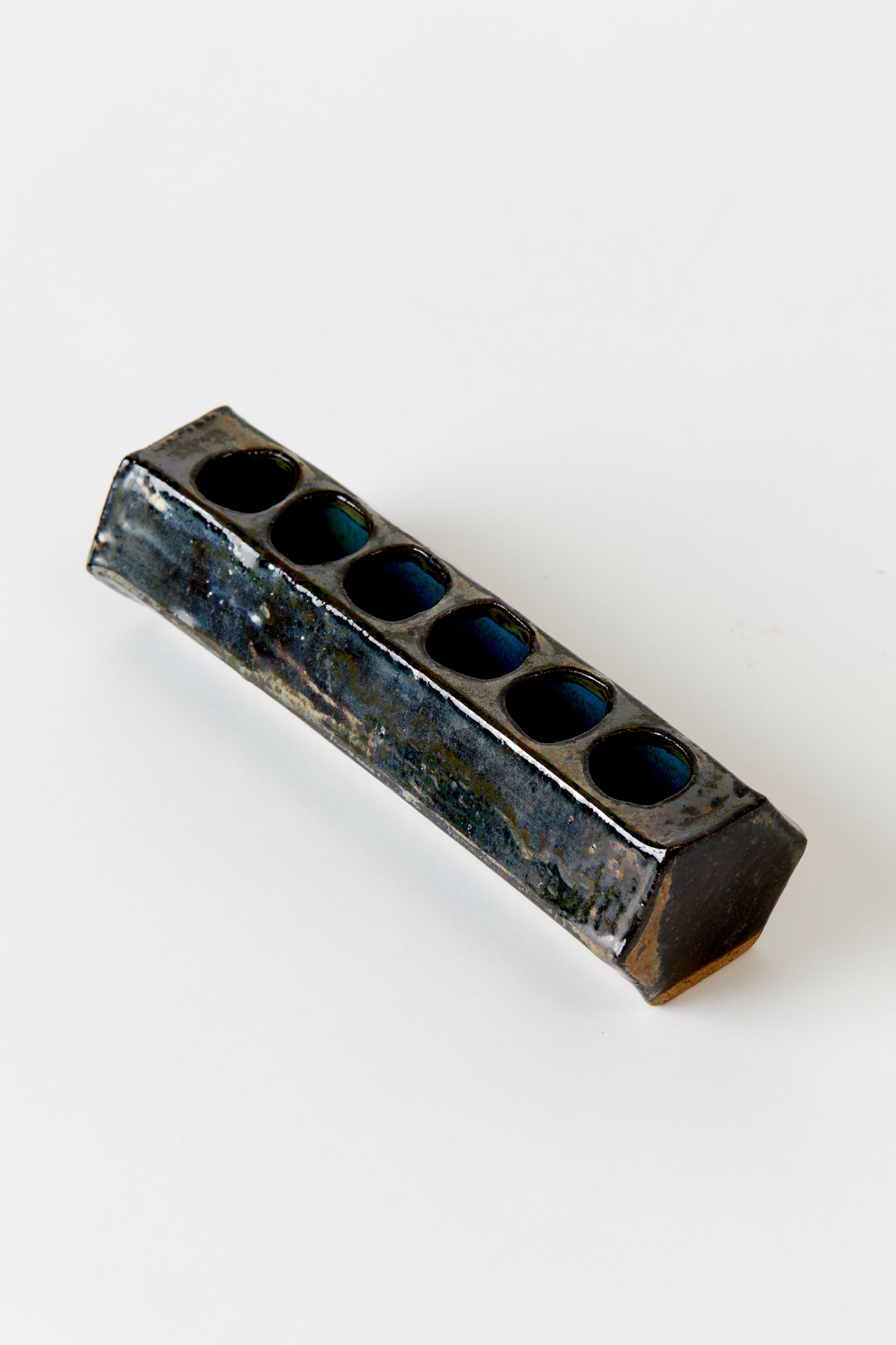 Vintage ceramic vase. Handbuilt ceramic hexagonal tube with 6 holes for flowers. Coated in a dark blue glaze with variation in color. 8" long by 2" tall.