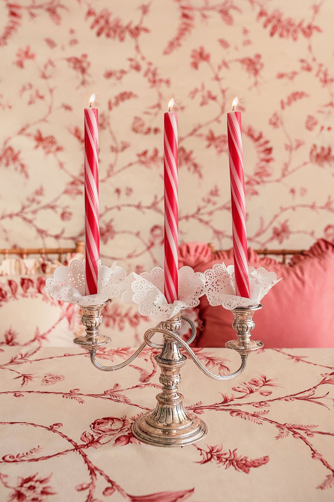 Set of three 12 inch taper candles with a red and white peppermint twist design, placed in a silver candelabra.