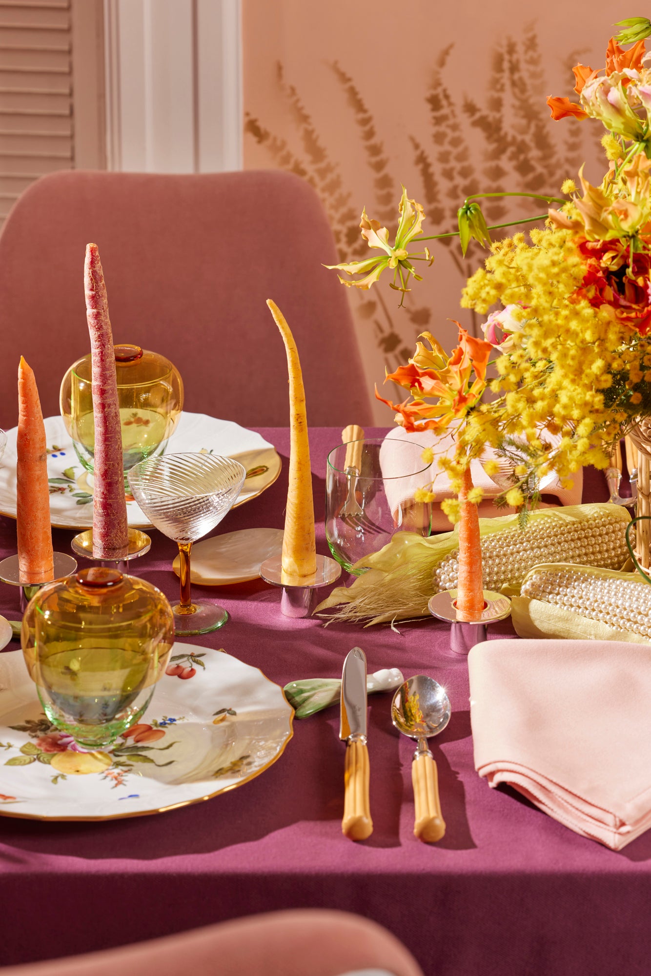 Lively Spring table scape with color block tablecloth in eggplant, majestic boxwood flatware, pearl corn, bamboo flatware, carrot taper candles, Nason Moretti coupe glass and 3 piece bowl, wine glass and water glass set.