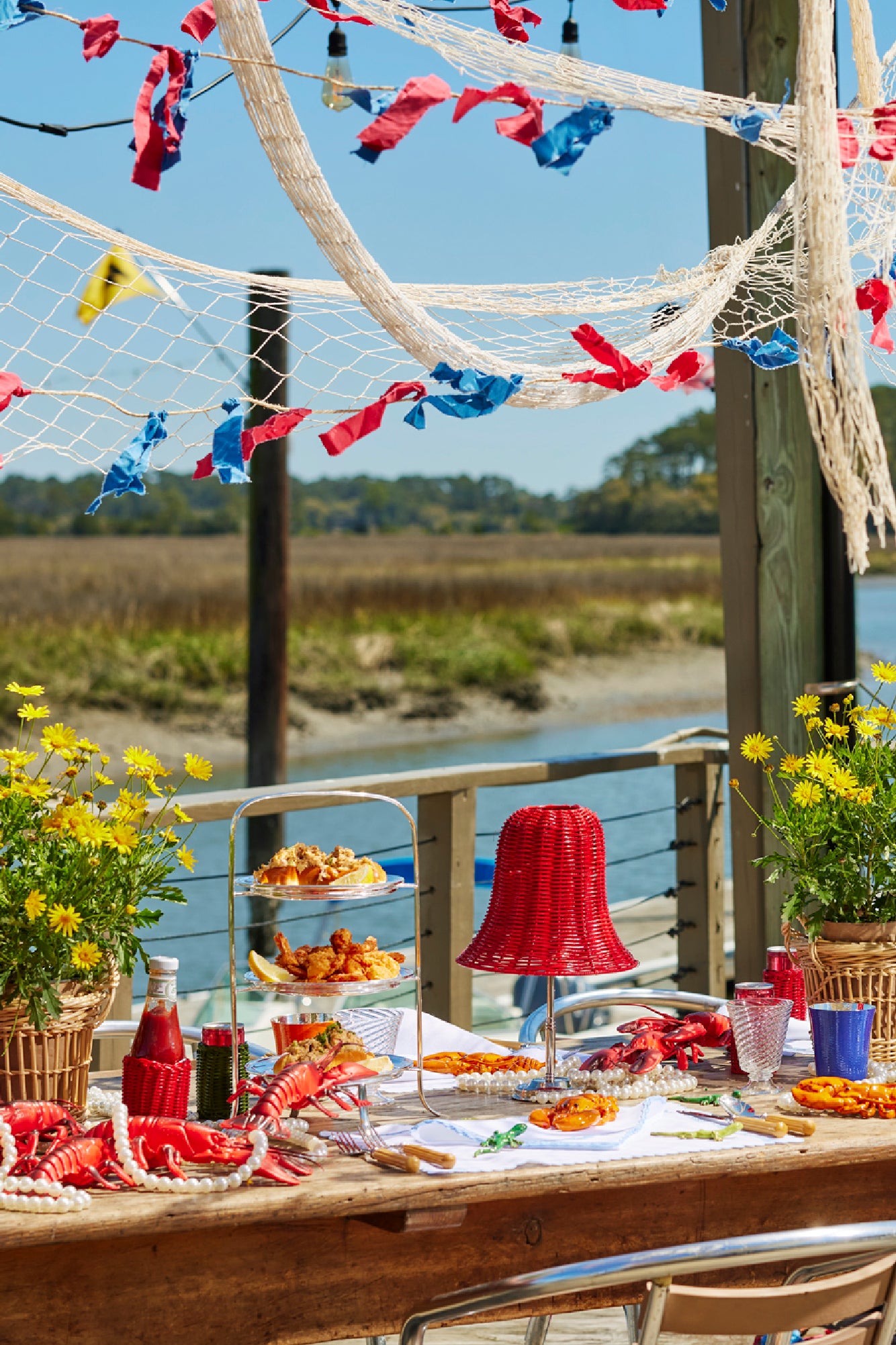 Summer tablescape with wicker lampshade, wicker basket, ceramic lobsters, and silver tea stand.