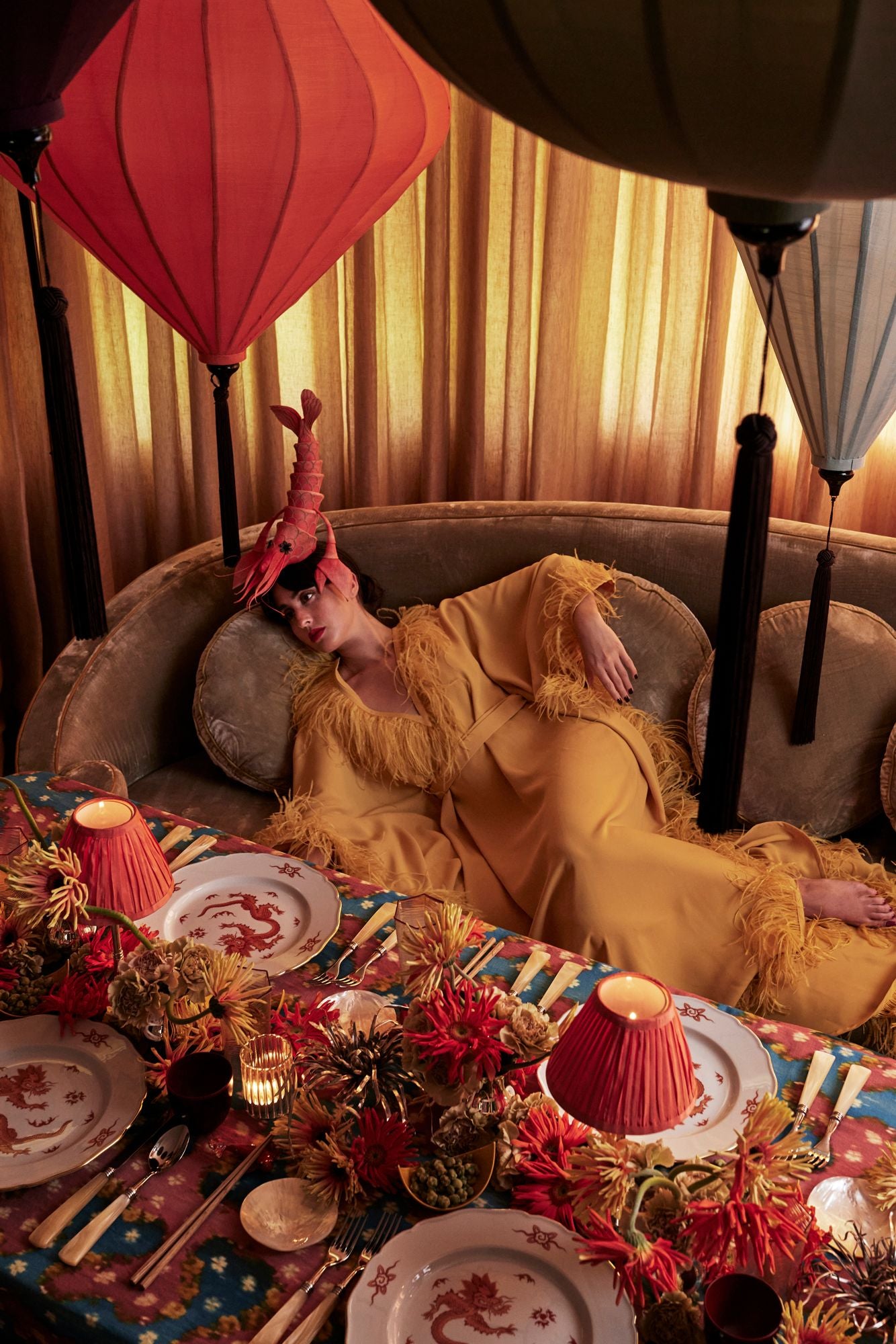 Woman in a yellow dress sitting on a couch with a decorated table in front of her, surrounded by colorful lanterns.