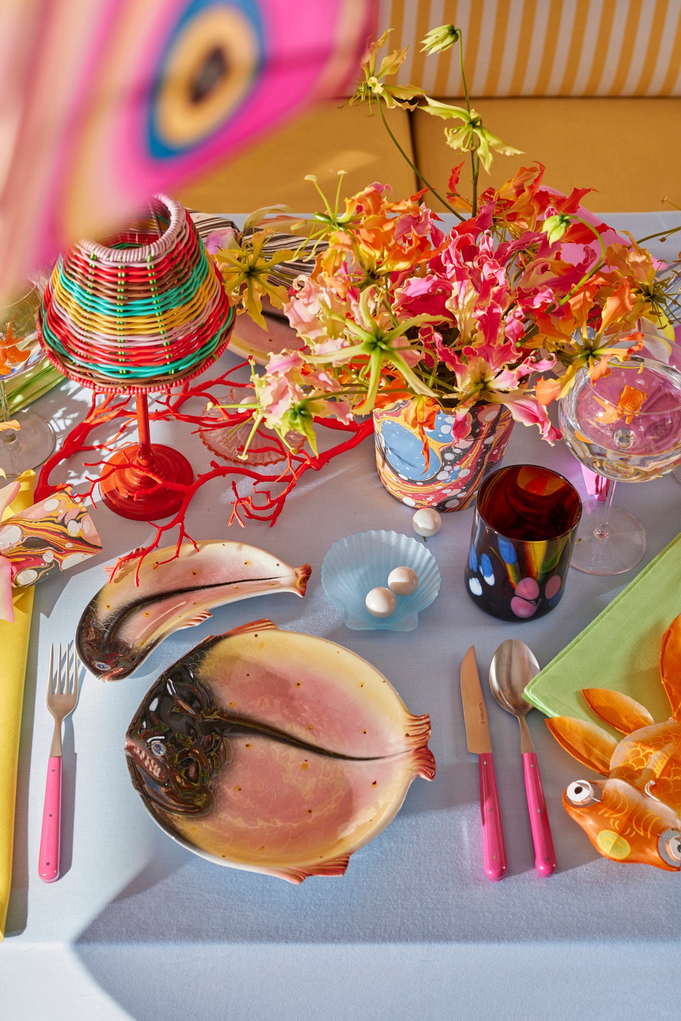 Under the Sea tablescape with marbled party crackers, color-block linens, woven lamp shade, and hot pink flatware.