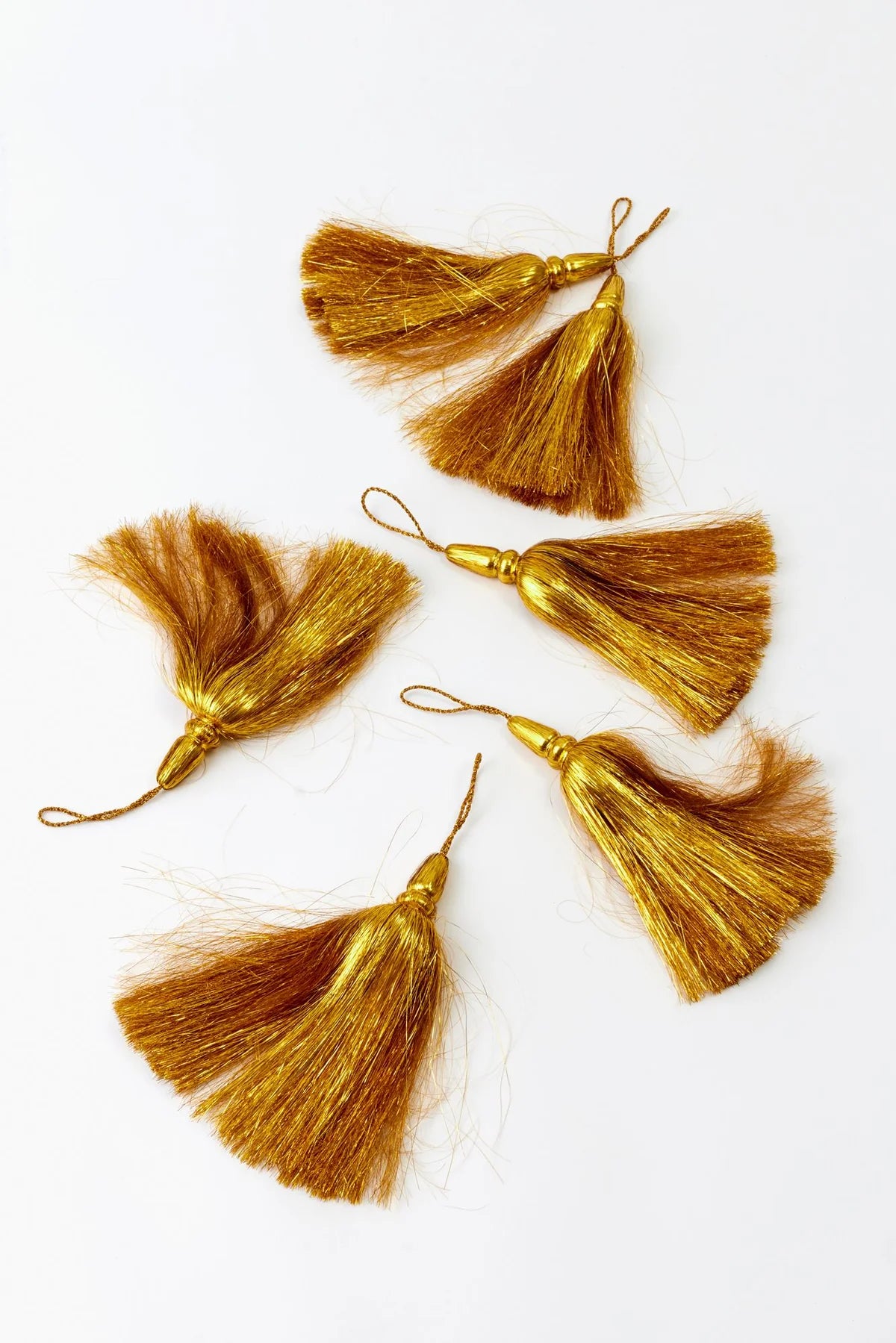 6 gold tassel embellishments made of shiny silk-like threads, arranged on a plain white background.