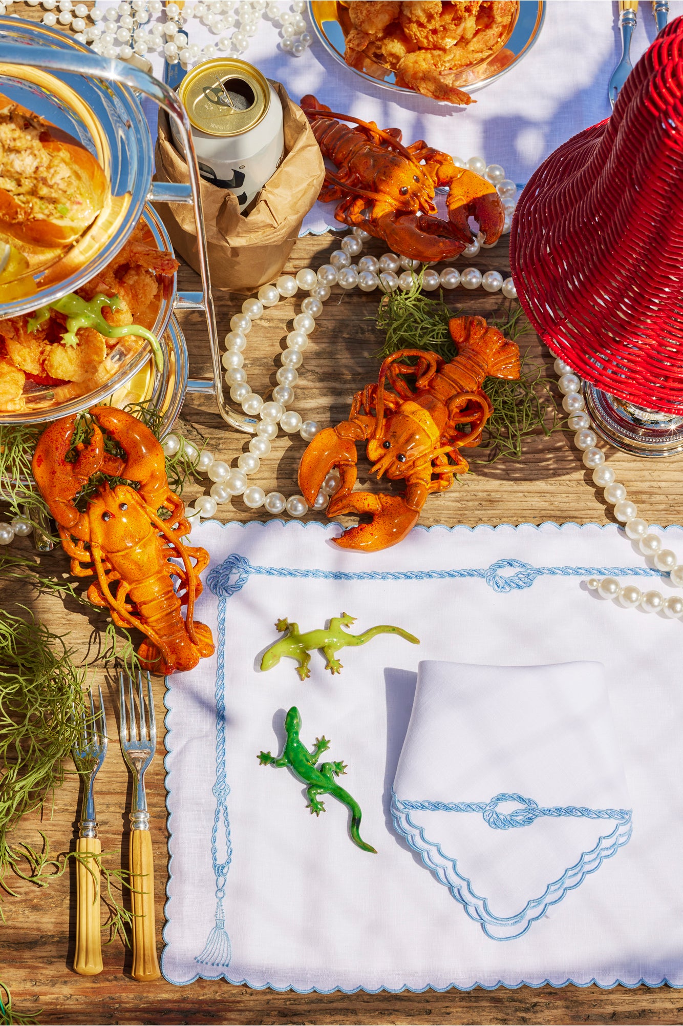 Summer tablescape with wicker lampshade, wicker basket, ceramic lobsters, and silver tea stand.