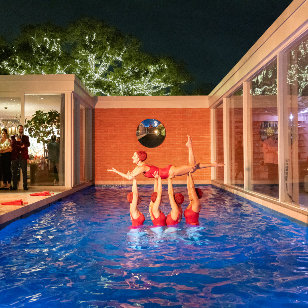 Swimmers in a pool at night with a building and trees in the background