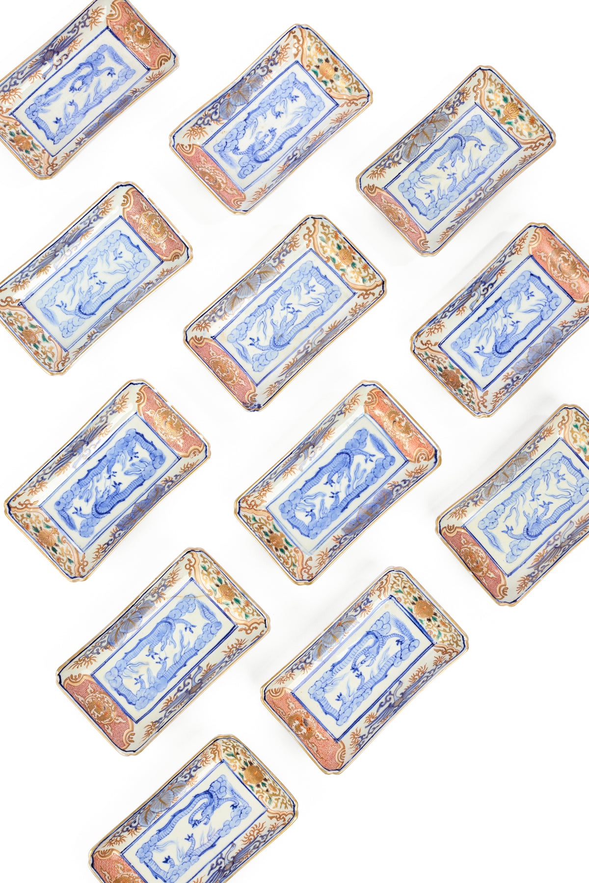 A set of 12 rectangular ceramic dishes with blue and white floral center panels with dragons and ornate orange, brown, and blue patterned borders, arranged diagonally on a white background.