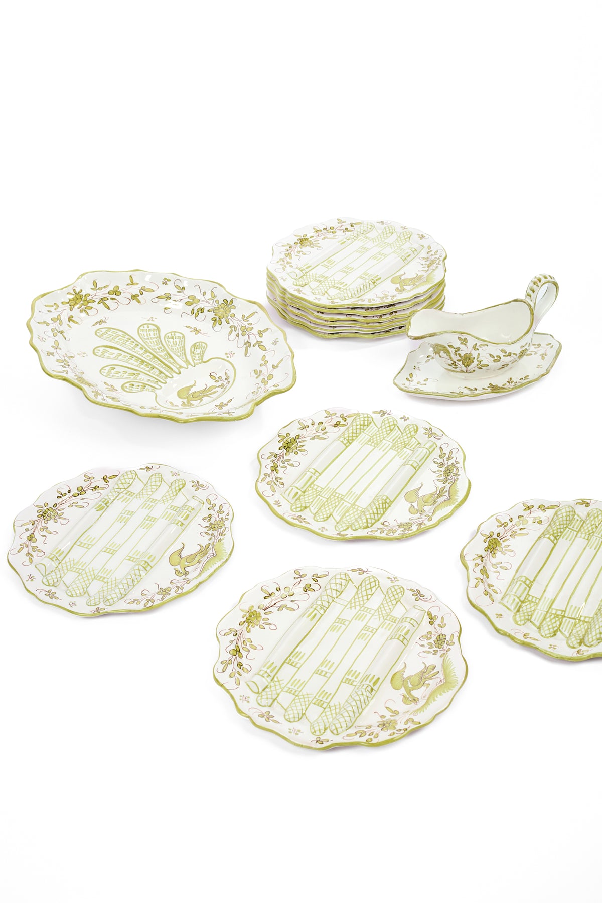 A set of white ceramic serving plates and a matching sauce boat and platter with a pale yellow-green floral pattern and etchings of asparagus, arranged on a clean white background.