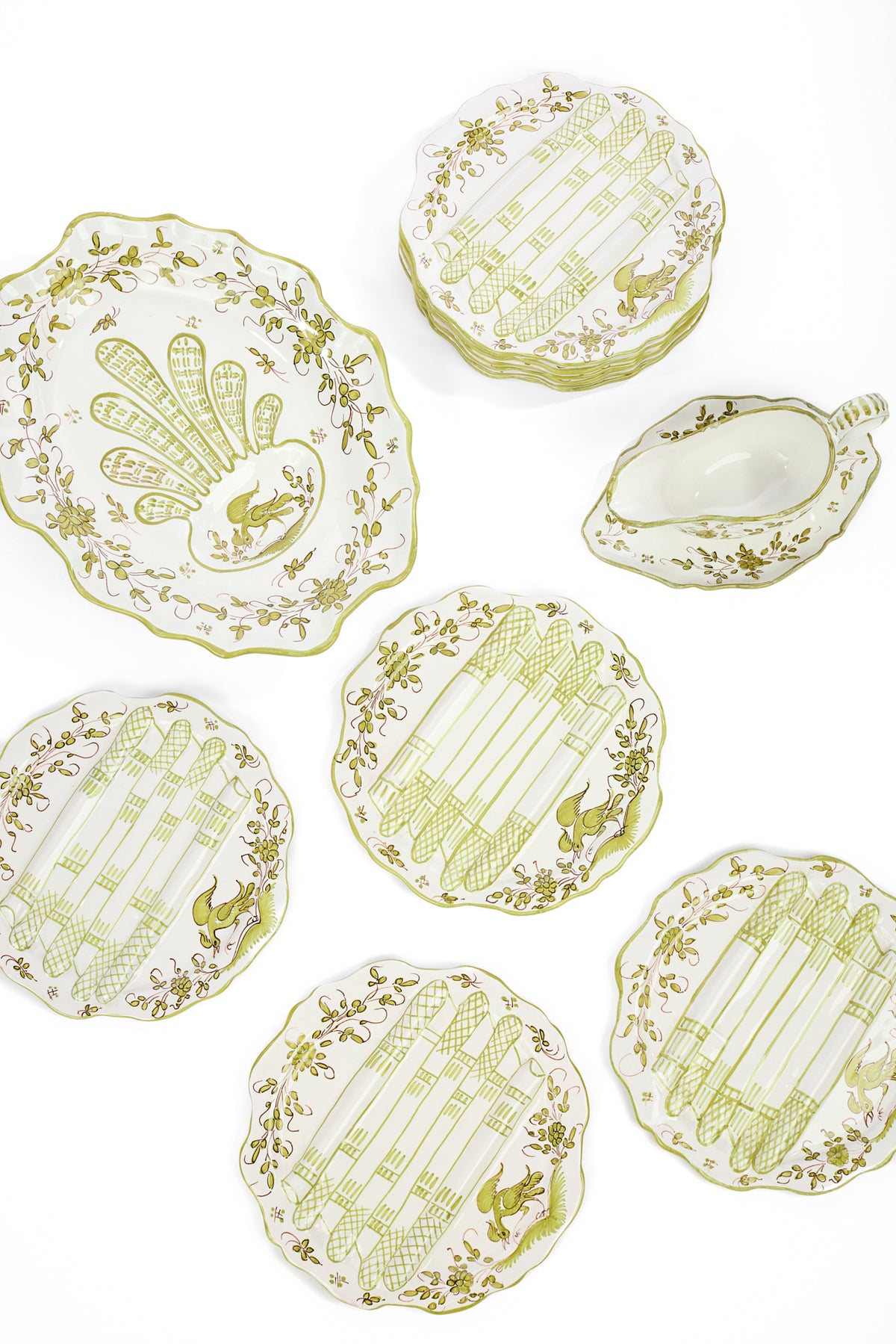 A set of white ceramic serving plates and a matching sauce boat and platter with a pale yellow-green floral pattern and etchings of asparagus, arranged on a clean white background.