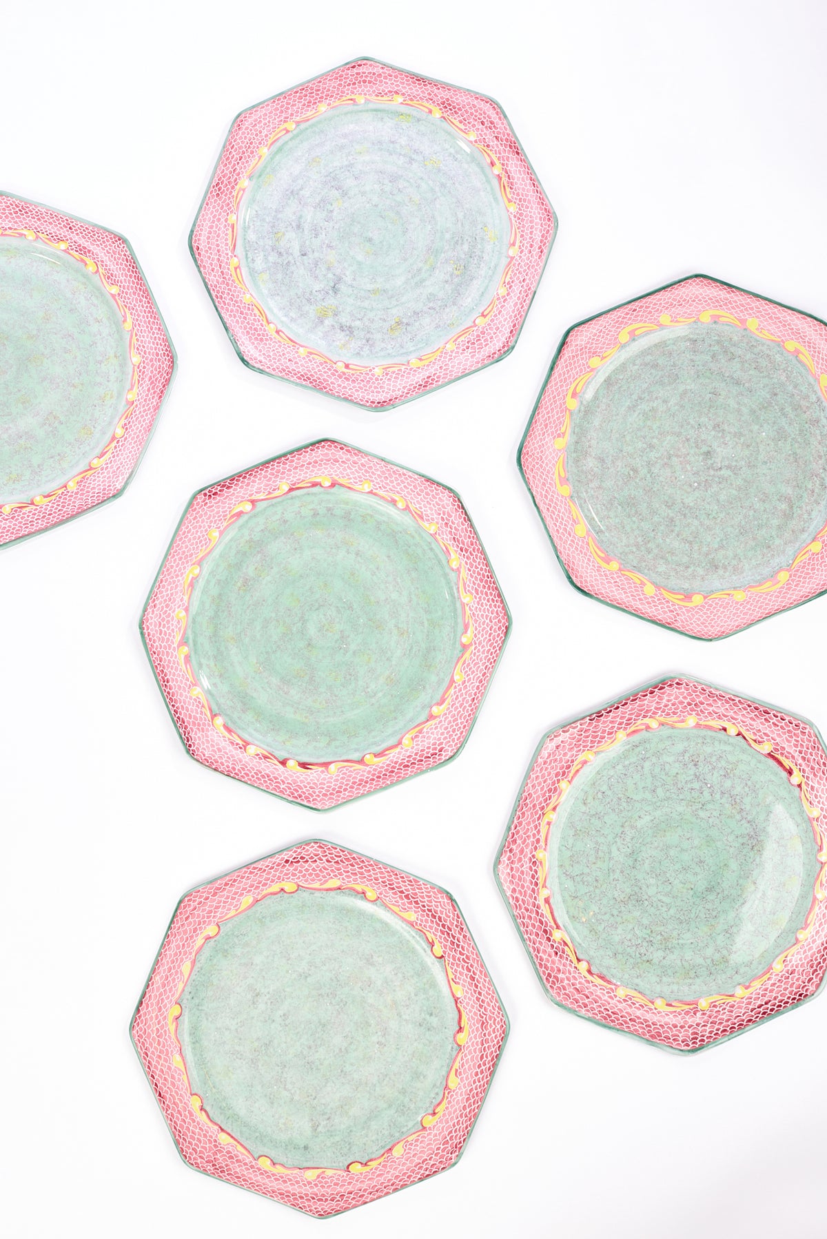 Set of 6 octagonal ceramic plates with a celadon green center and reddish pink scale patterned border with bits of gold on the edged against a white backdrop.
