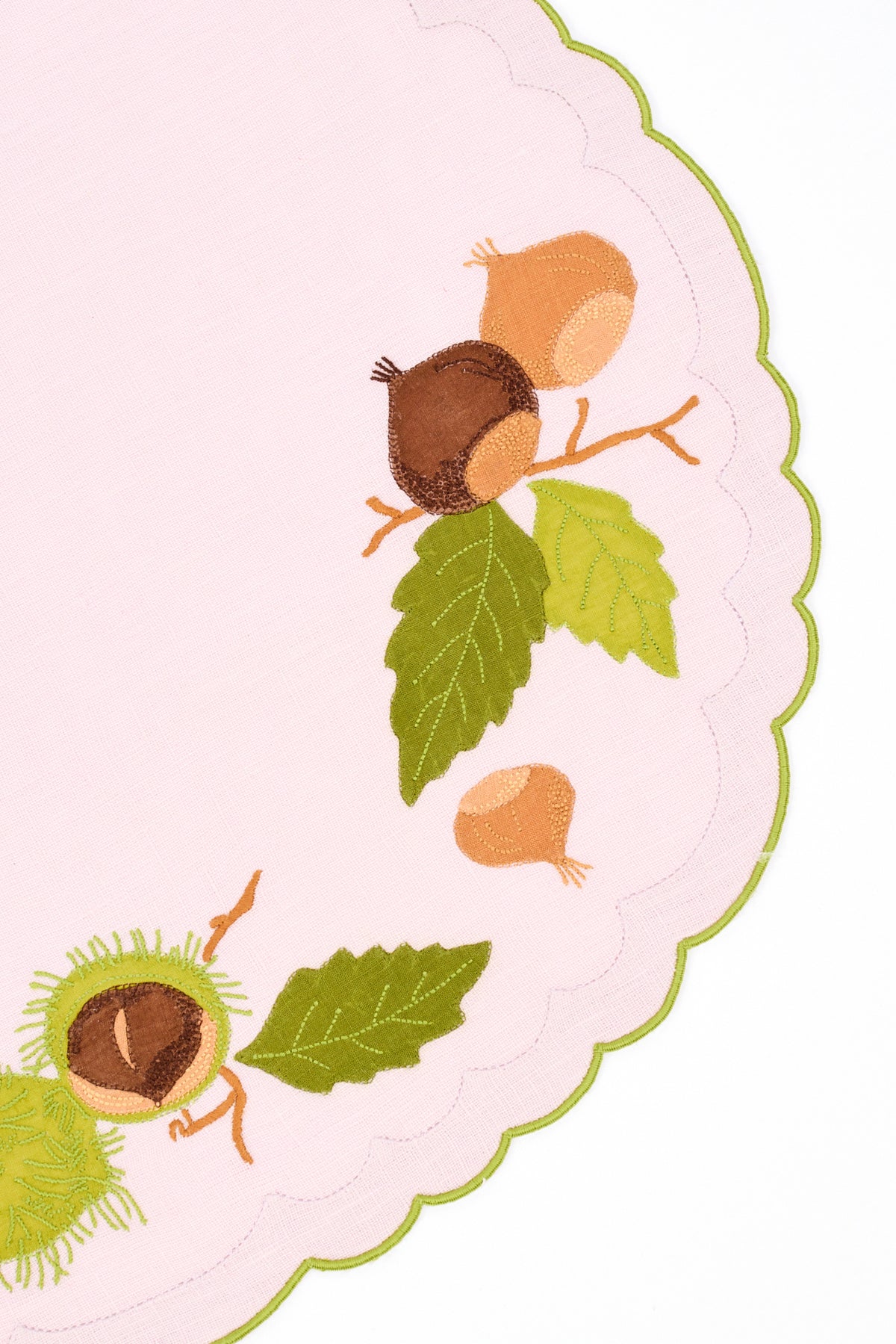 Pink scalloped linen placemat with green stitched border. Hand stitched brown and green chestnut appliqués loosely patterned on top.