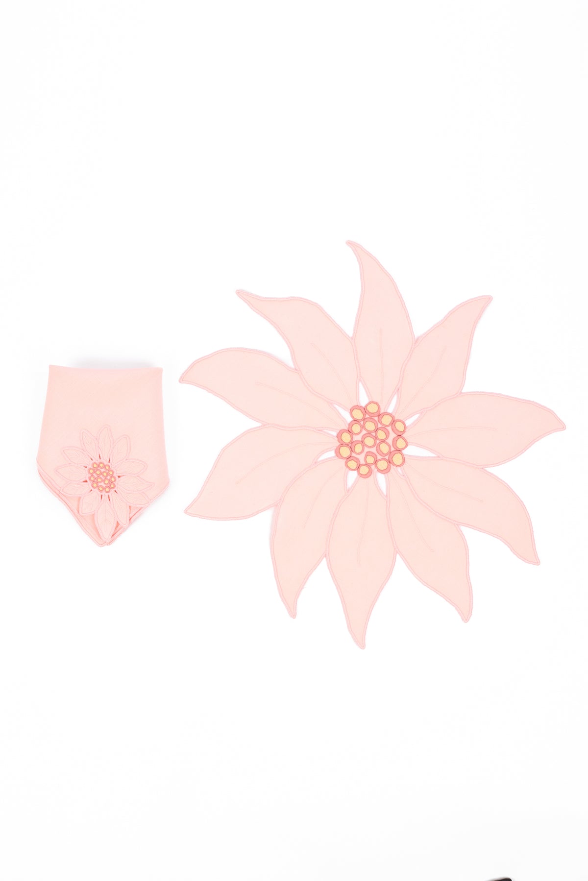 A poinsettia-shaped fabric napkin and place mats  in pale pink, arranged on a plain white background.