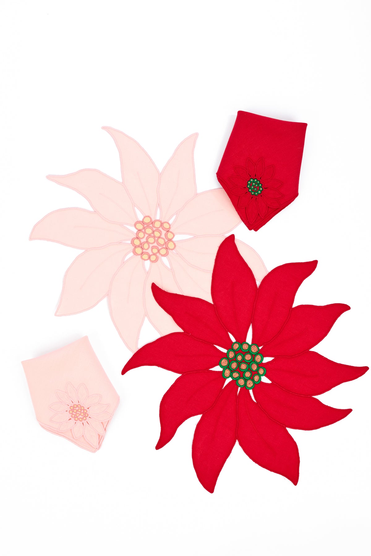 Two poinsettia-shaped fabric napkins and place mats  in red and pale pink, arranged on a plain white background.