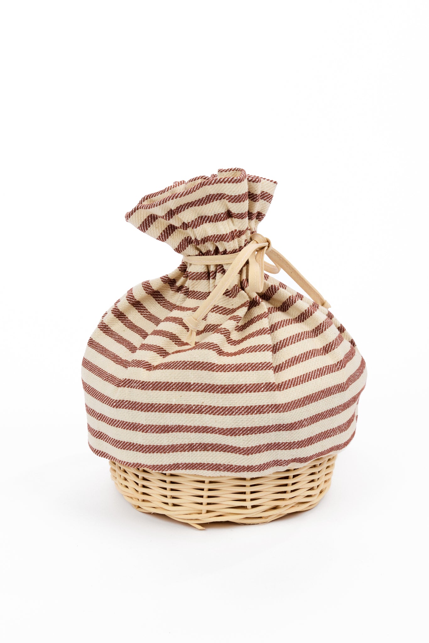 A fabric drawstring pouch with brown and cream horizontal stripes, tied and gathered at the top, resting on a small natural wicker basket against a plain white background.