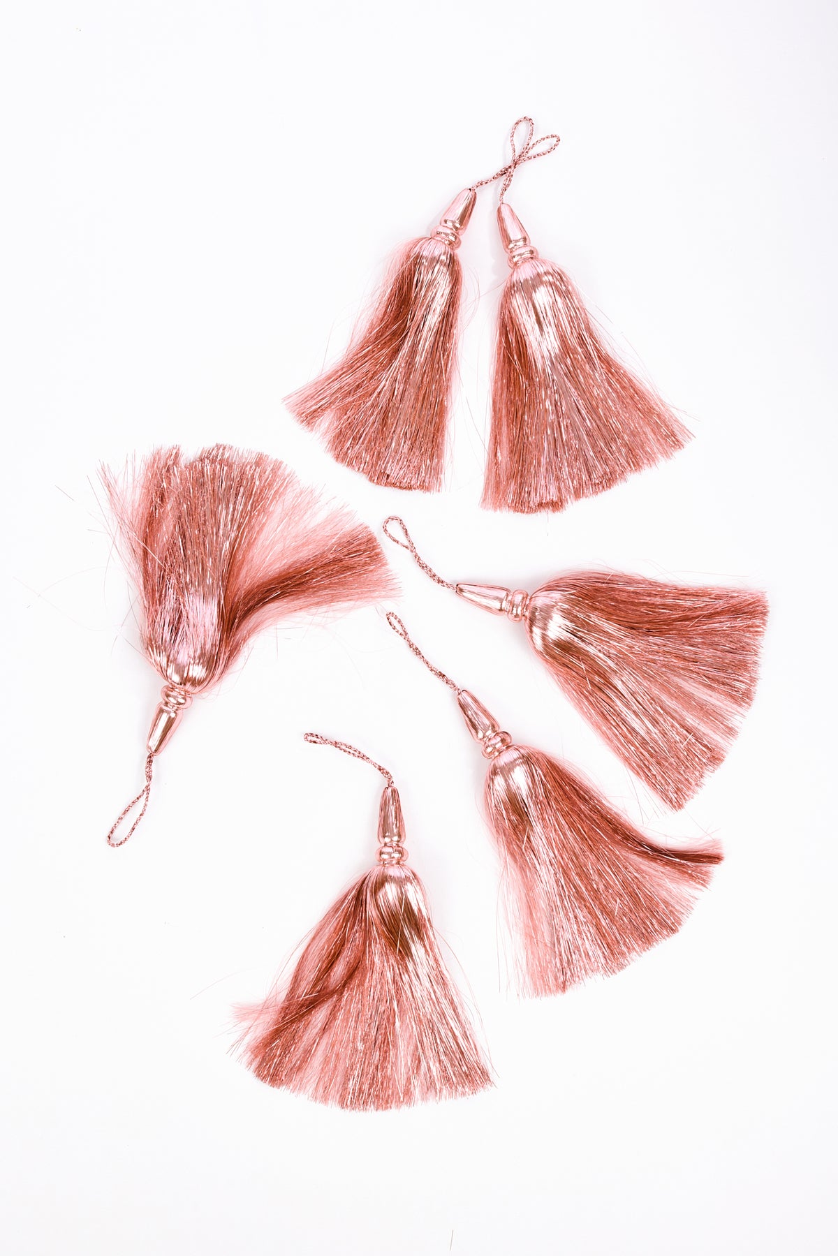 6 rose gold tassel embellishments with attached loops, arranged on a plain white background.