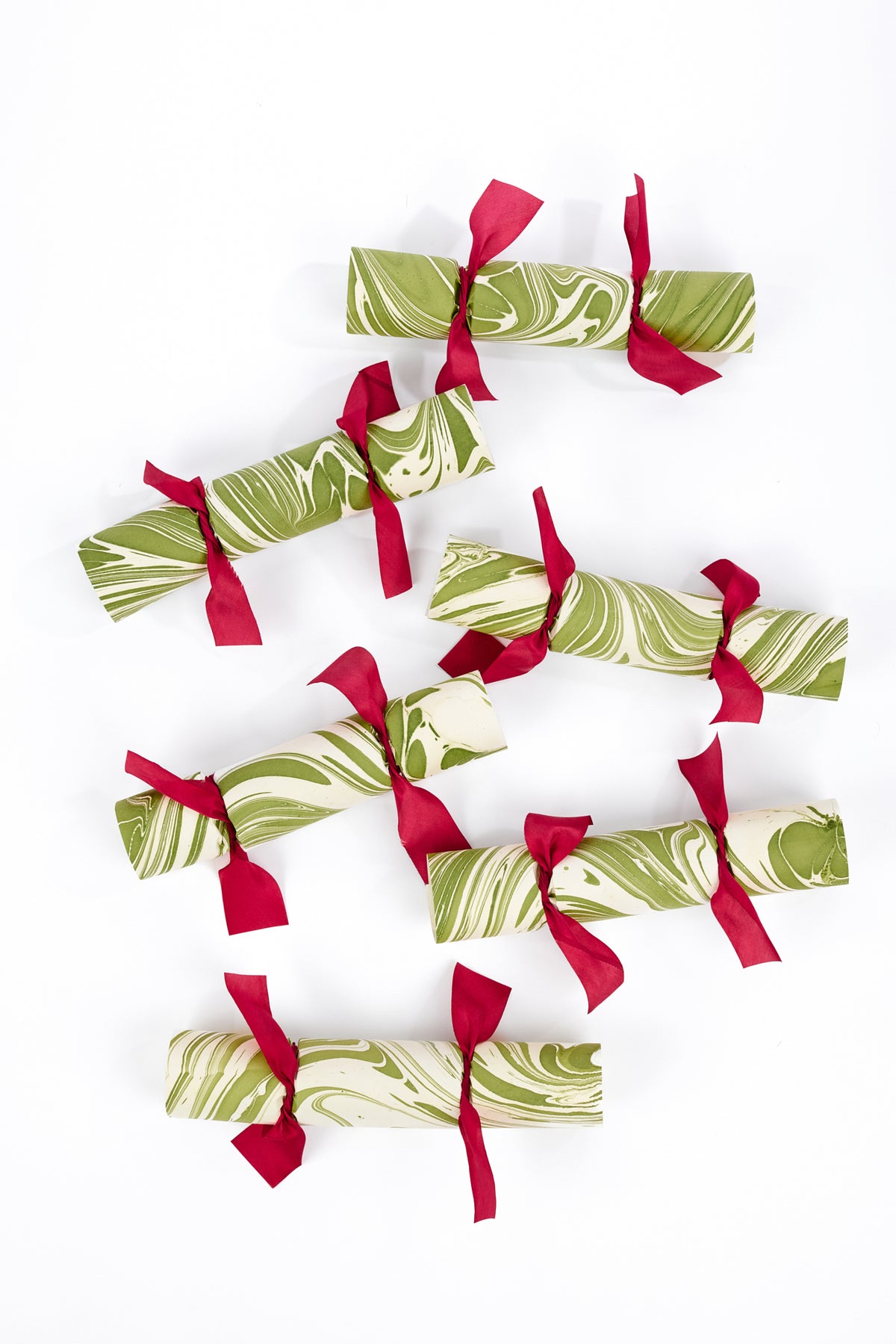 Six Christmas crackers arranged on a plain white background. Each cracker features a green and cream marbled pattern with a red ribbon tied at the center.