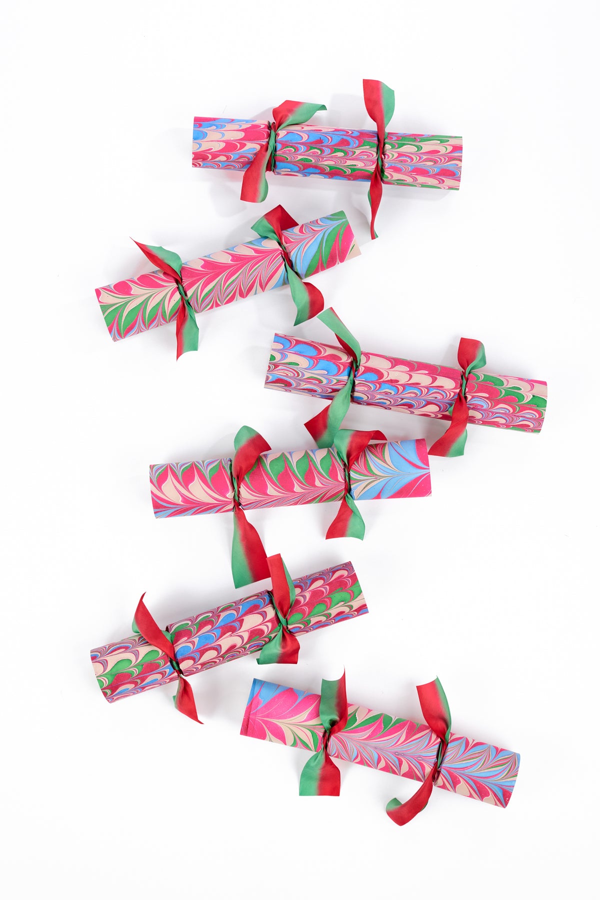 Six marbled paper Christmas crackers with red and green ribbon ties, arranged vertically on a clean white background.