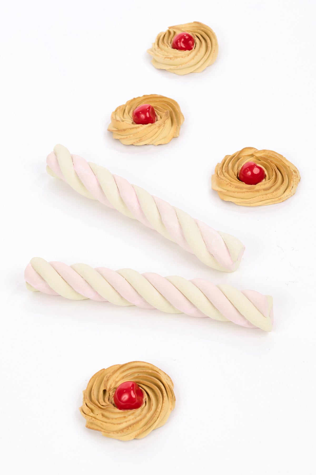 Faux Porcelain Italian swirled cookies with faux glossy red cherries and faux porcelain spiraled pale pink marshmallow sticks against a clean white backdrop.