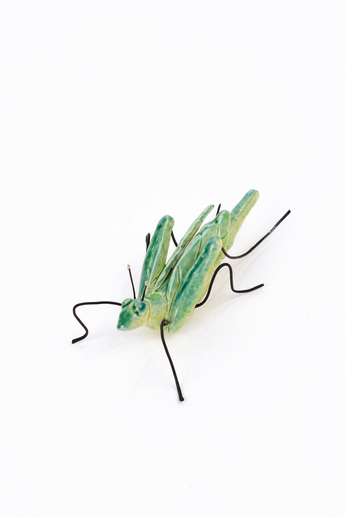A green grasshopper figurine with black legs and antennae, photographed on a plain white background.