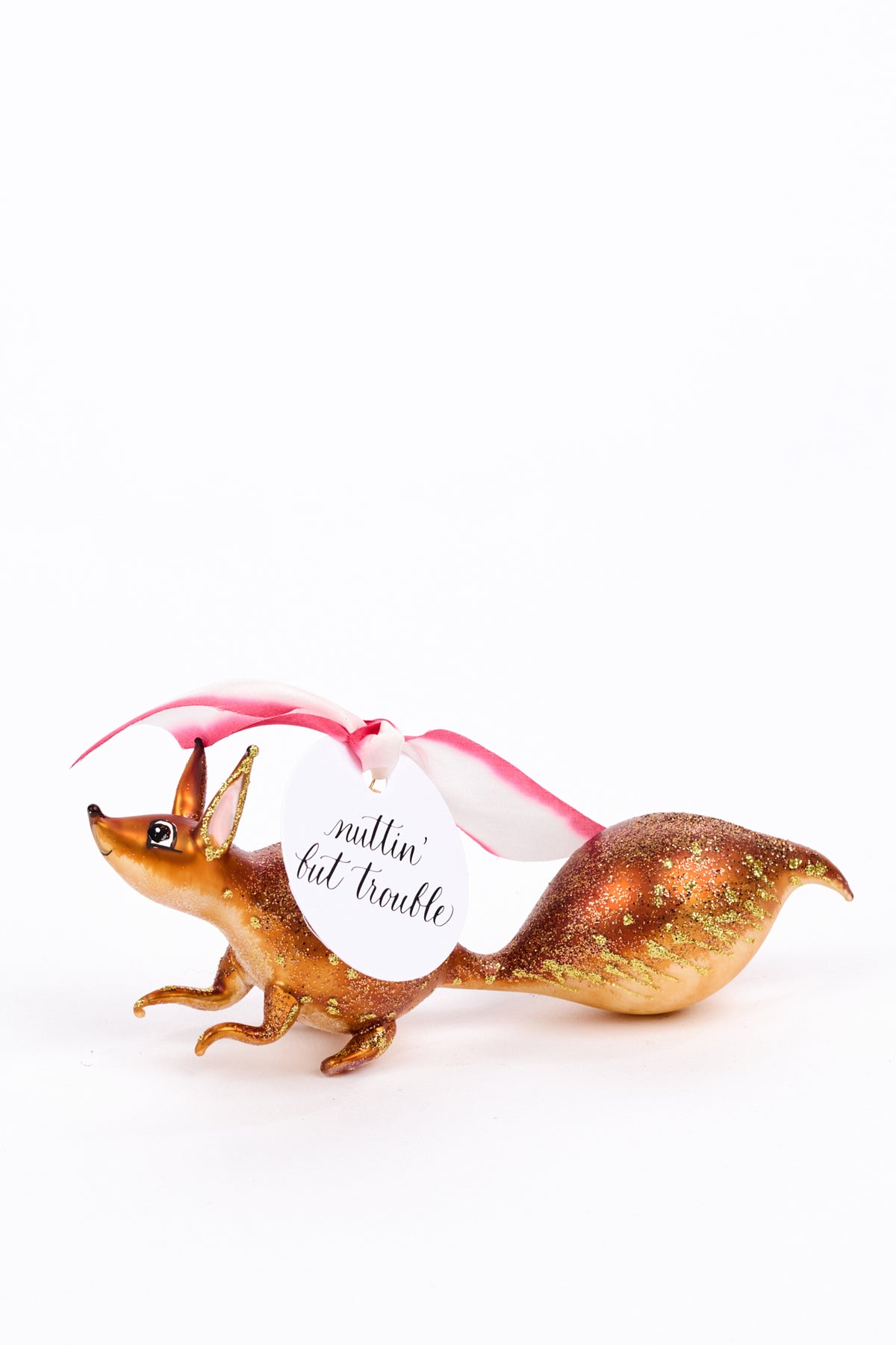 A decorative ornamente of a brown and gold squirrel with a pink and white ribbon and a hanging white tag that reads 'nuttin' but trouble', photographed on a clean white background.