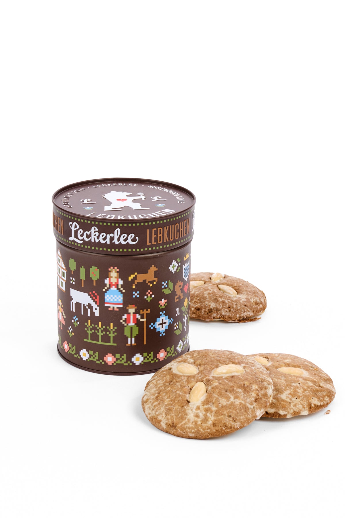A Leckerlee Lebkuchen round metal tin with a colorful folk-art design, shown next to three round Lebkuchen cookies on a clean white background.