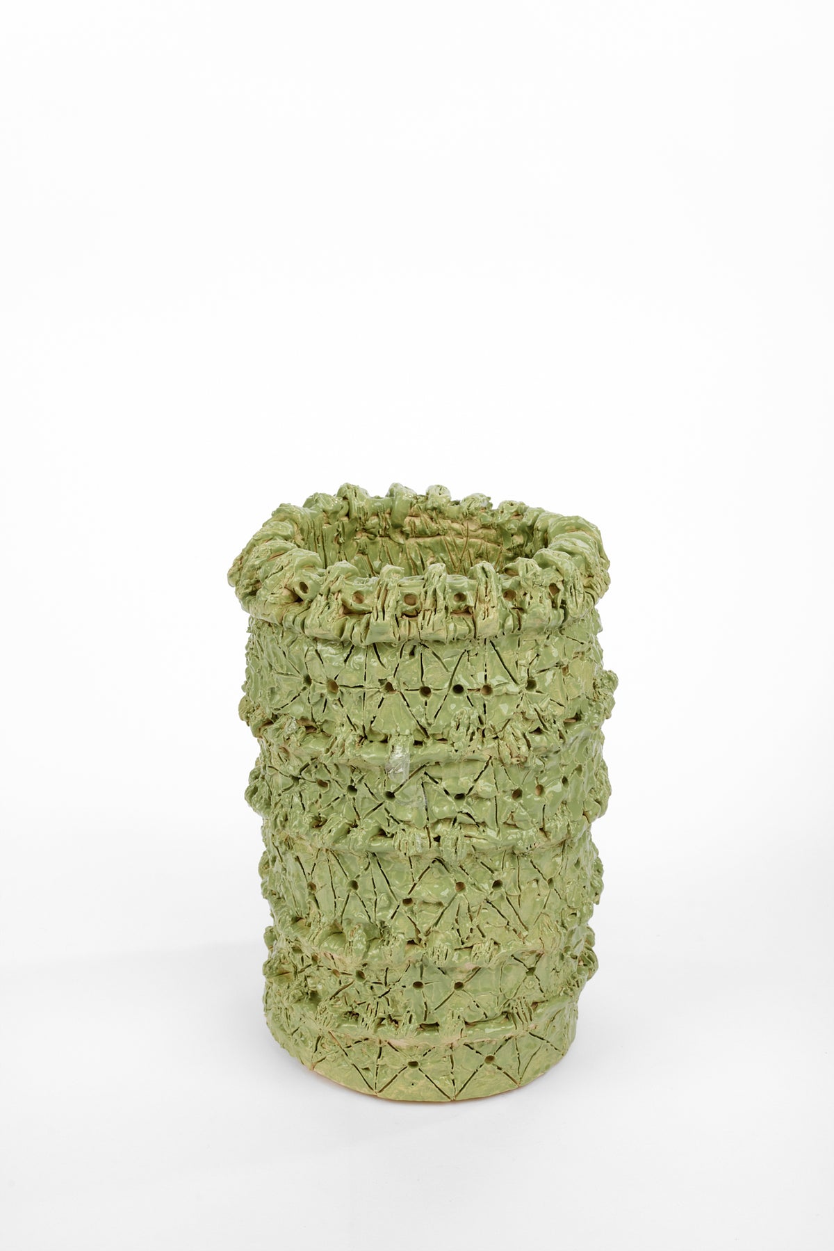 Cylindrical pale green ceramic vase with an uneven rim and a heavily textured surface. Layered horizontal bands are covered with incised lines, small holes, raised knots, and roughly formed clay details.