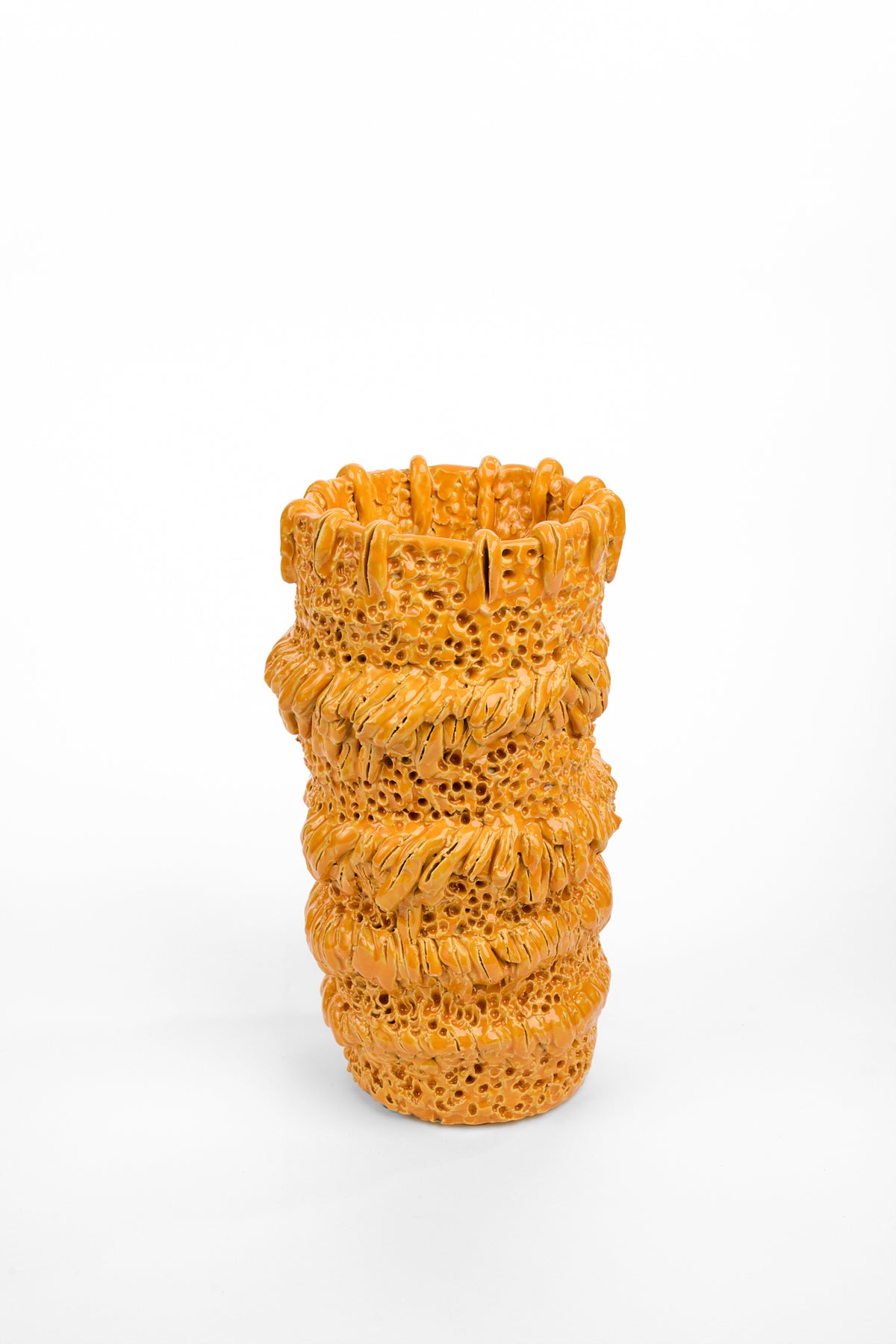 Cylindrical orange ceramic vase with an irregular rim and deeply textured surface. Alternating bands of small holes and thick, gathered ridges wrap around the vase from top to bottom.