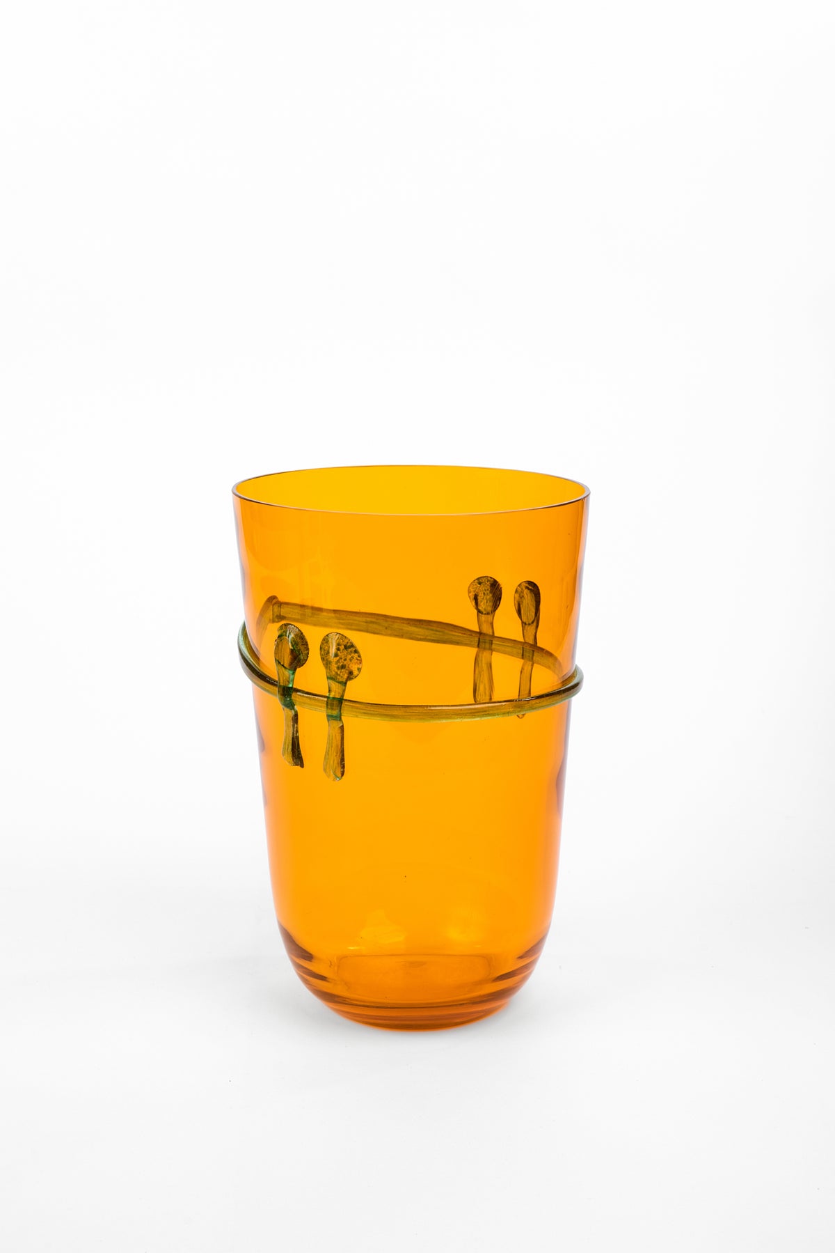 An amber orange translucent glass tumbler with a decorative band of small dark green spoon motifs around the middle, set against a plain white background.