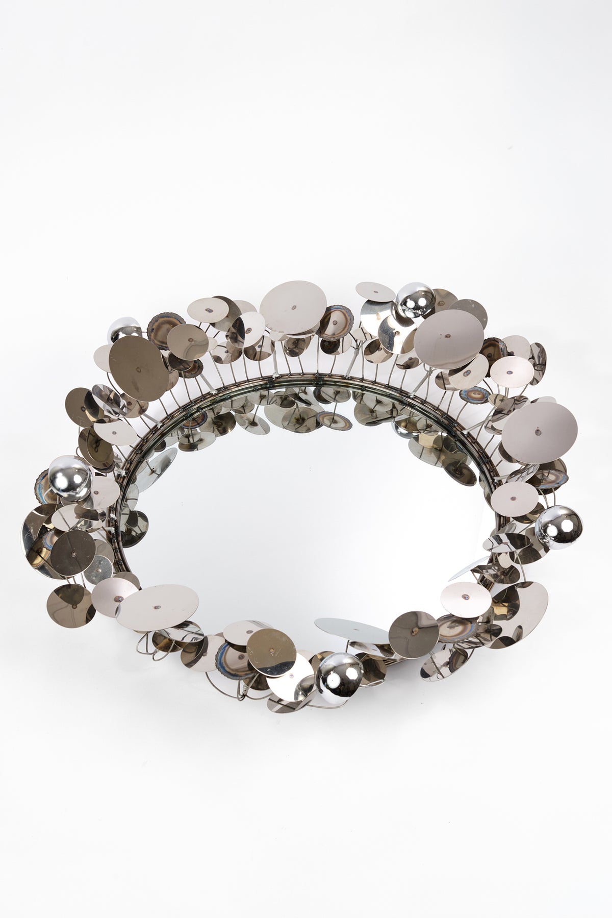 A circular mirror framed with dense, reflective silver sequins and metallic discs, photographed on a clean white background.