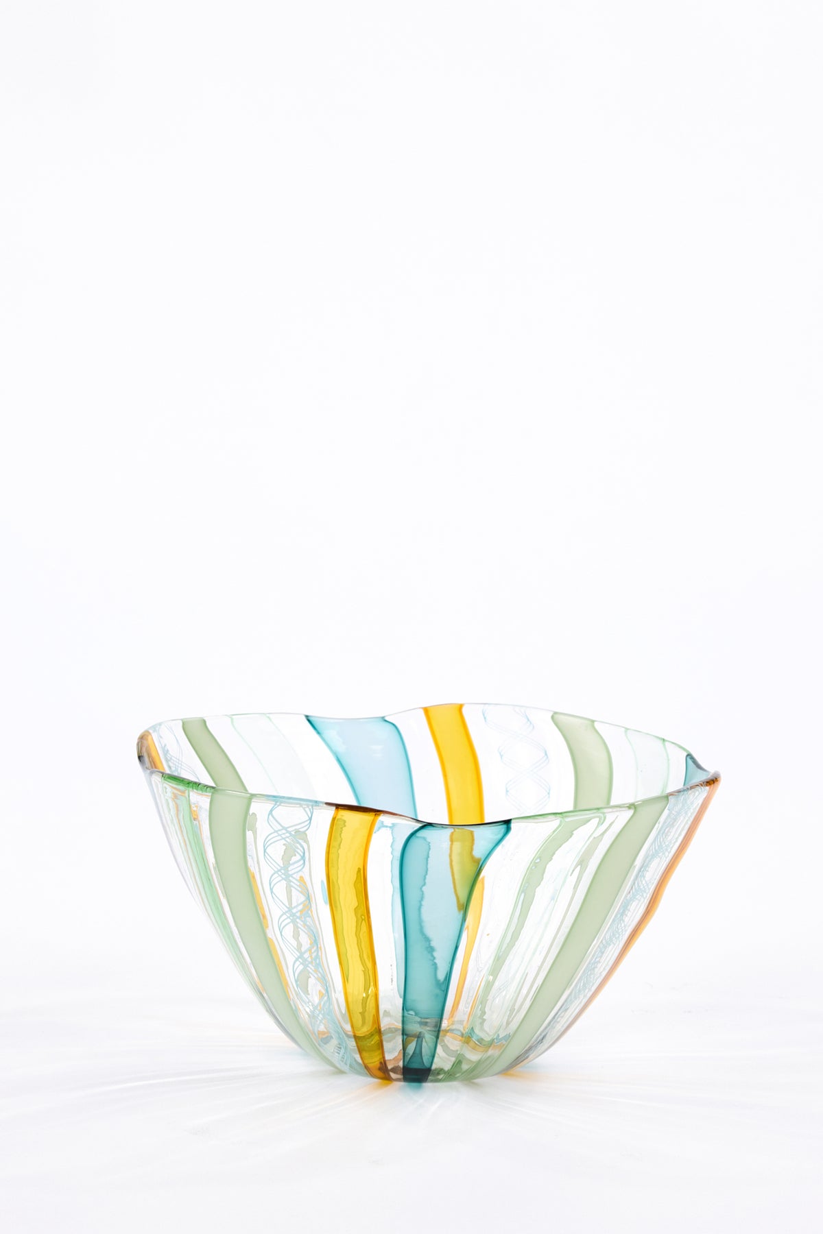 A hand-blown glass bowl with vertical stripes of yellow, teal blue, sage green, and white, set against a seamless white background.
