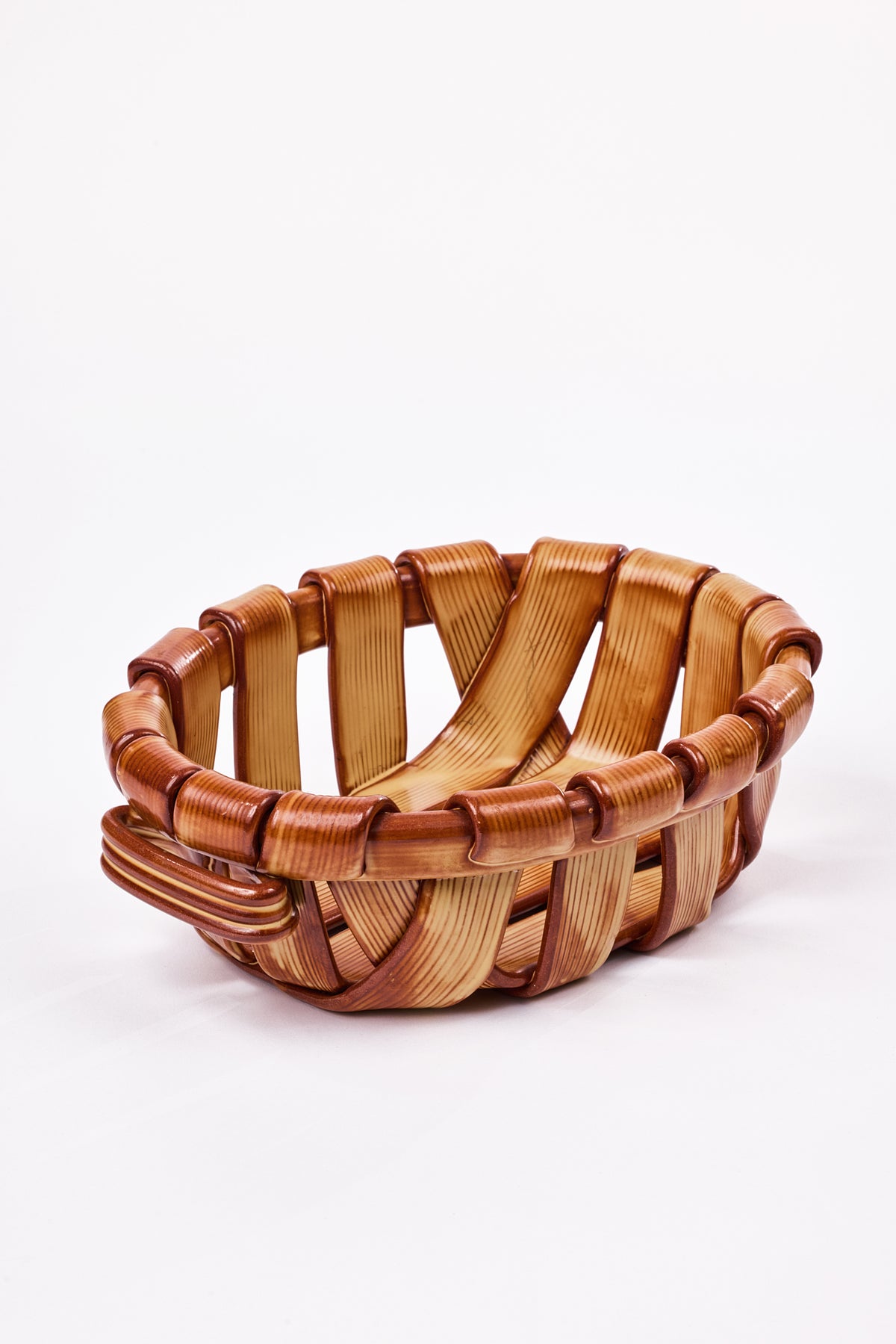 A ceramic serving basket made to look like an oval woven basket made from interlaced natural wood strips, shown on a clean white background.