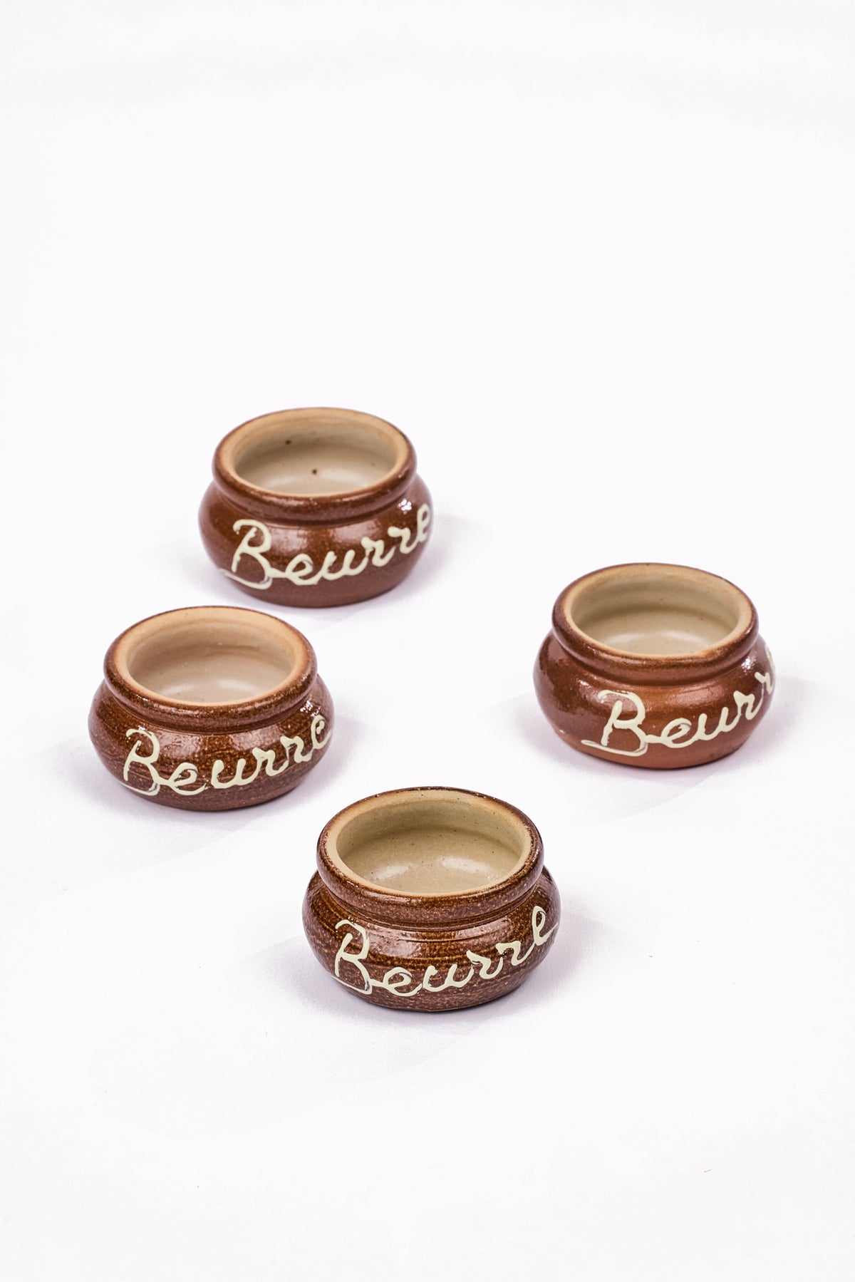 Set of four brown glazed French looking pots with white script reading "Beurre"