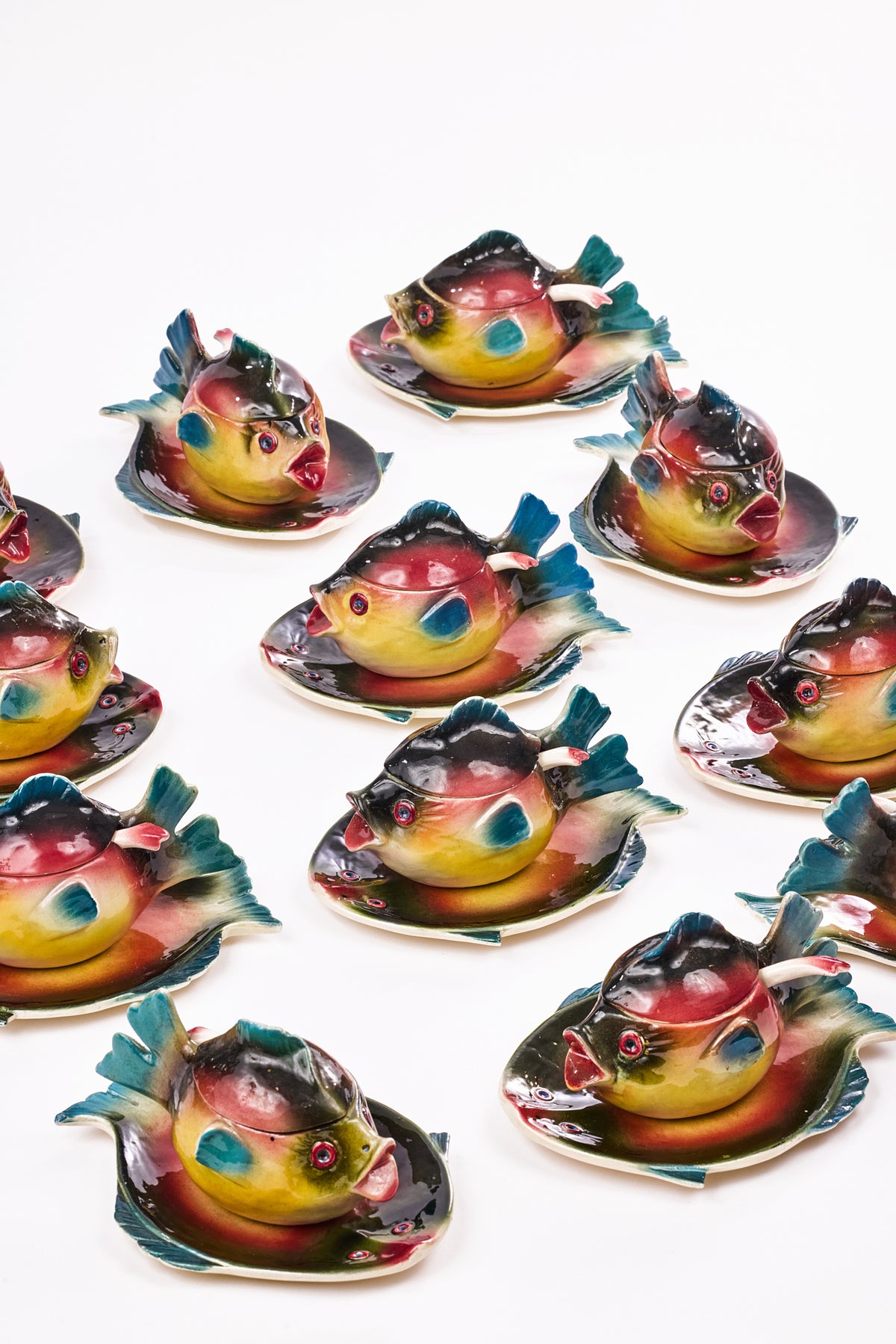 A set of colorful ceramic fish-shaped dishes  arranged on a plain white background. Each fish figure has a glossy finish with black, red, yellow, blue, and green painted details, and sits on a matching fish-shaped saucer.