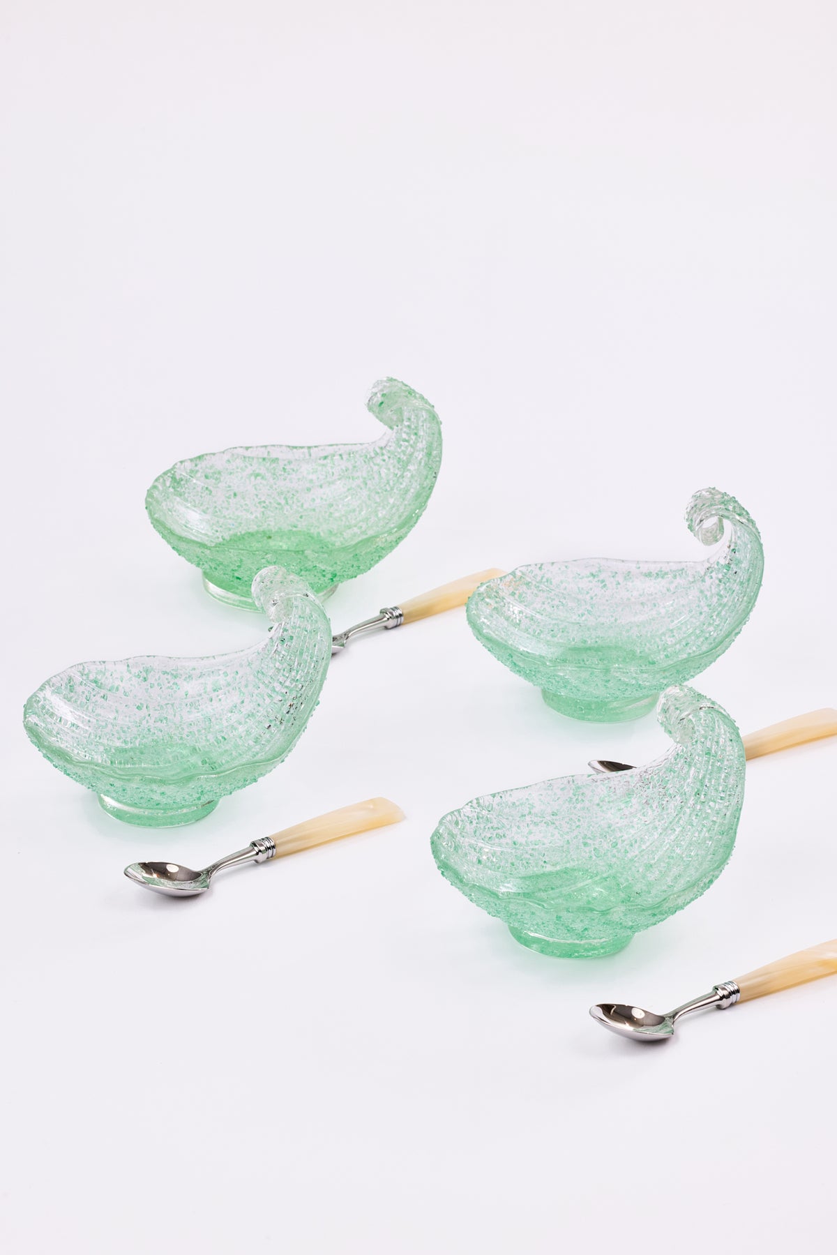 Four light green shell-shaped bowls with silver-toned metal spoons that have pale natural pearl handles, arranged on a clean white background.