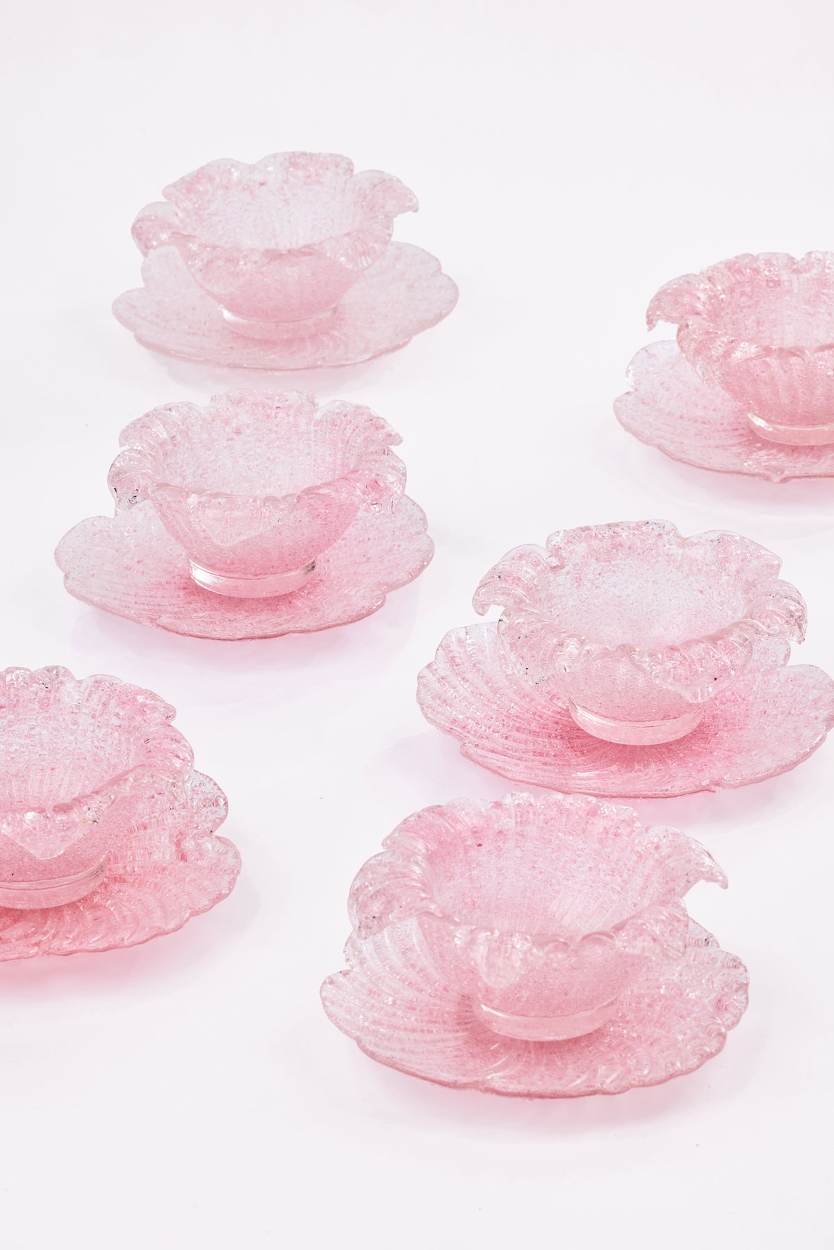 Six pink textured glass flower-shaped bowls with matching saucers, arranged on a clean white background.