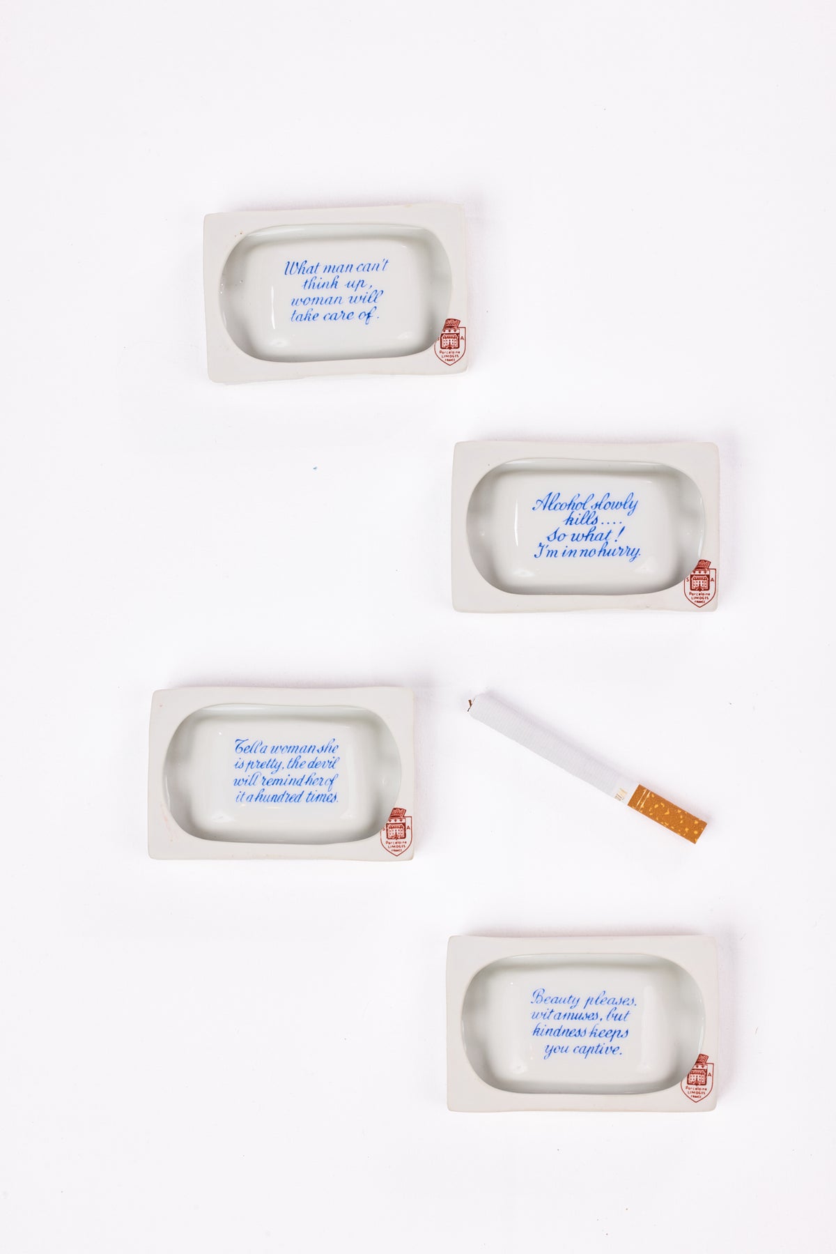 Four white porcelain ashtrays with blue handwritten quotes and small red wax seals, arranged on a white background with a single cigarette prop.