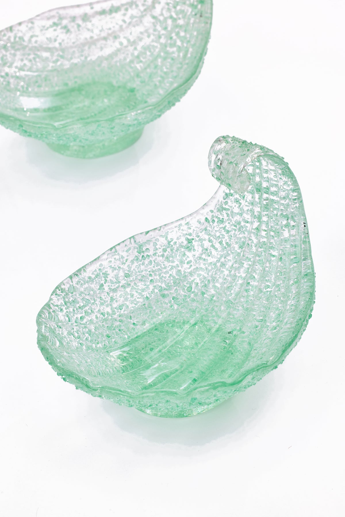 Two light green textured shell glass bowls on a clean white background, with one bowl in sharp focus in the foreground and another partially visible in the upper left.