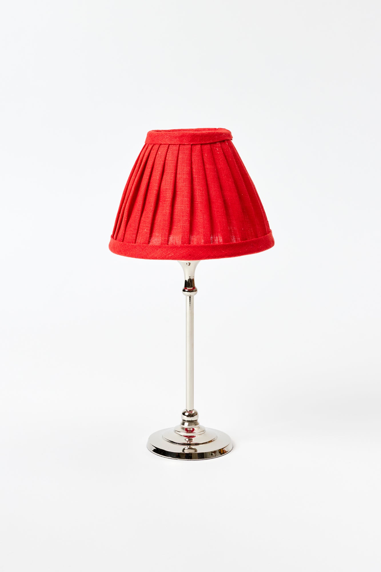 Small table lamp against a white background. Chrome colored lamp base with a bright red pleated silk lamp shade. 