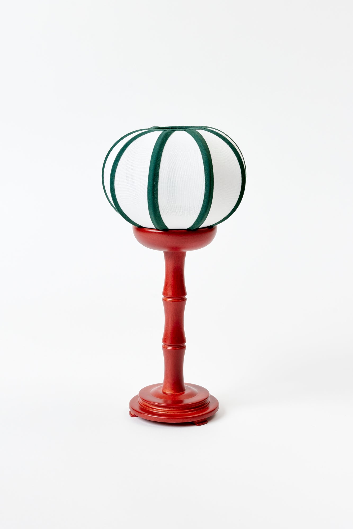 Table lamp against a white background, featuring a white shade with green trim, and a red base.