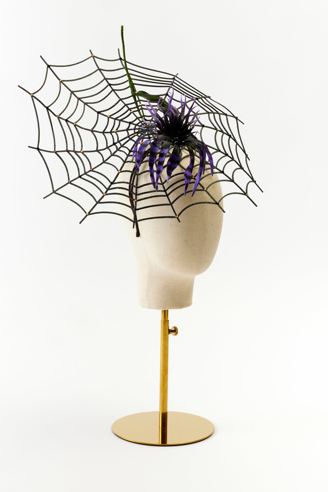 A dramatic spiderweb headpiece featuring a large black web extending outward, adorned with a striking black and purple striped flower at the center.