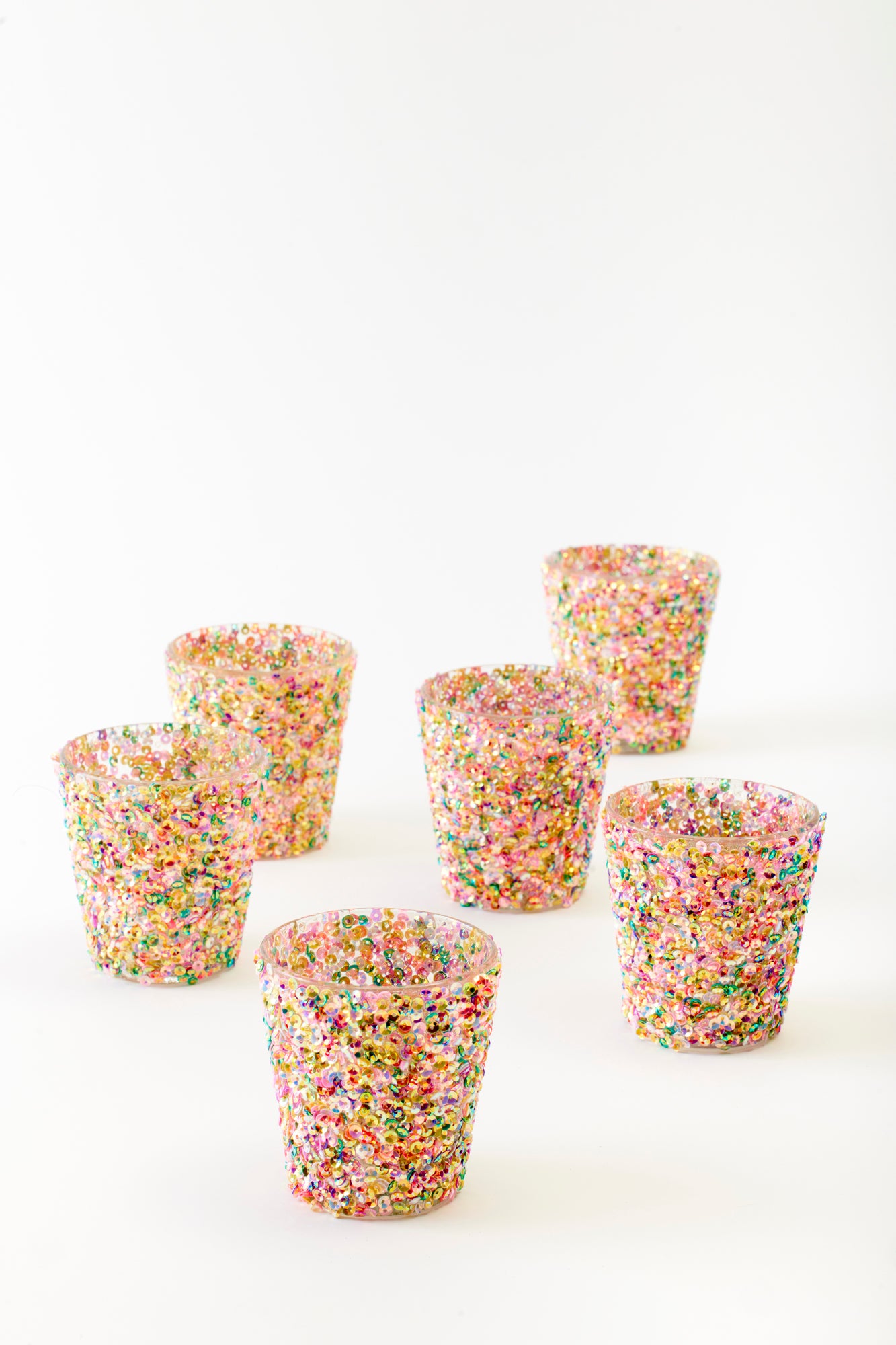 Set of six dazzling glass tumblers covered in multicolored sequins, shimmering with vibrant hues of pink, gold, green, and purple. These playful and glamorous glasses are the perfect statement pieces for a festive gathering, adding a touch of sparkle and celebration to any event.